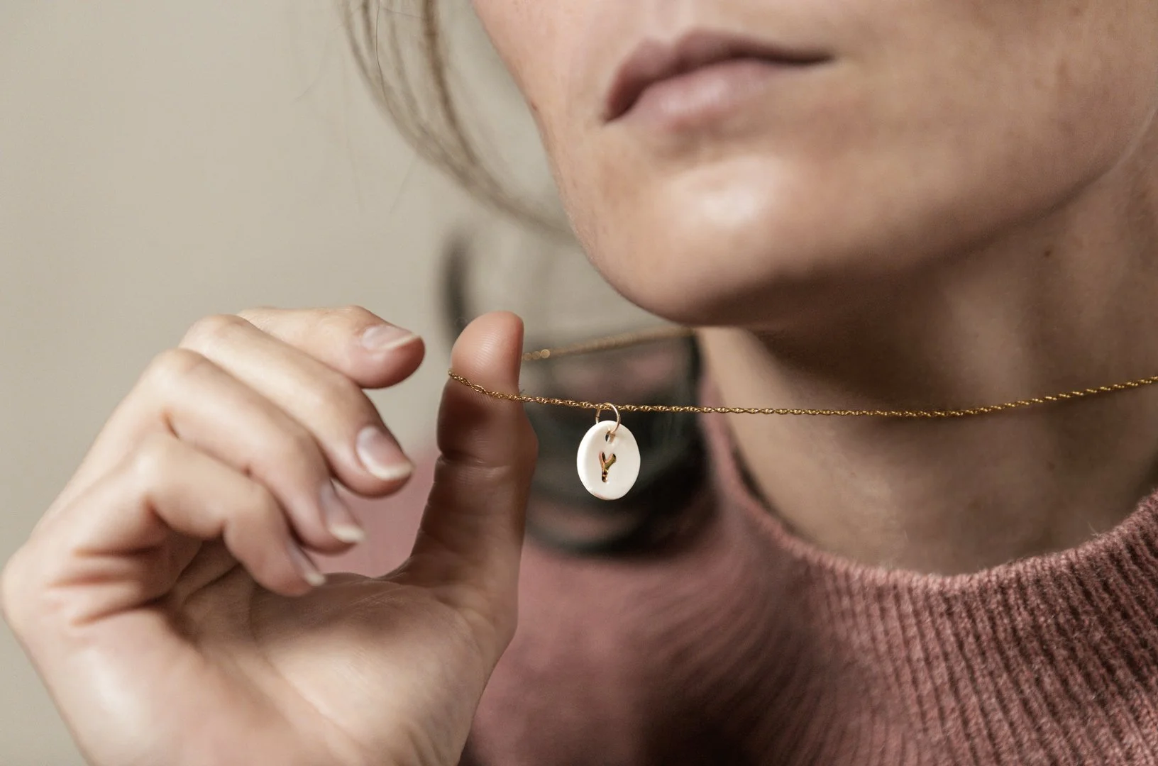 Close-up d'une femme tenant un collier doré avec un pendentif en forme d'oiseau blanc, conçu par l'atelier Moca.