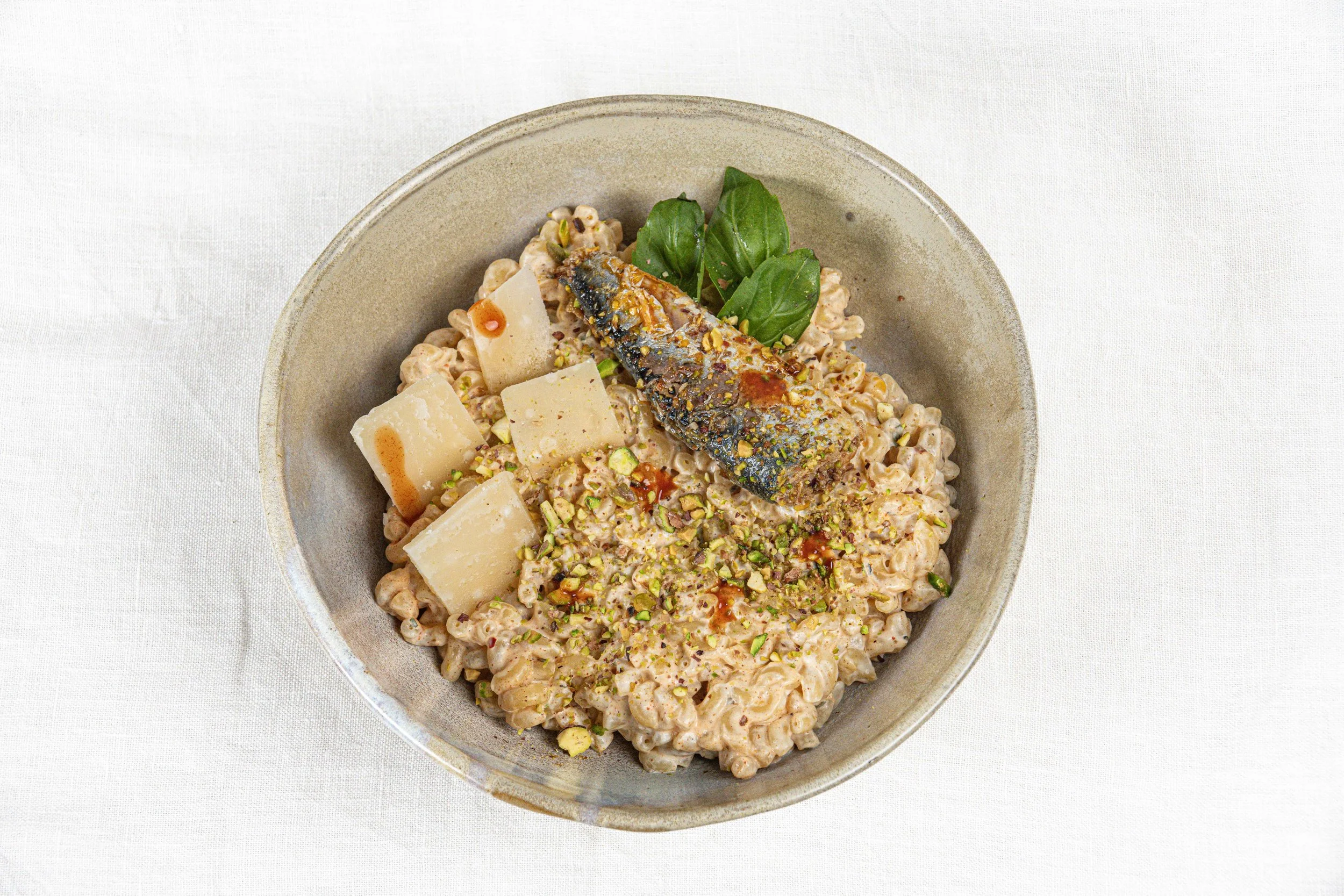 Bol de risotto crémeux garni de parmesan, pistaches, une tranche de poisson et quelques feuilles de basilic. Par le photographe culinaire Yves Daniel. 