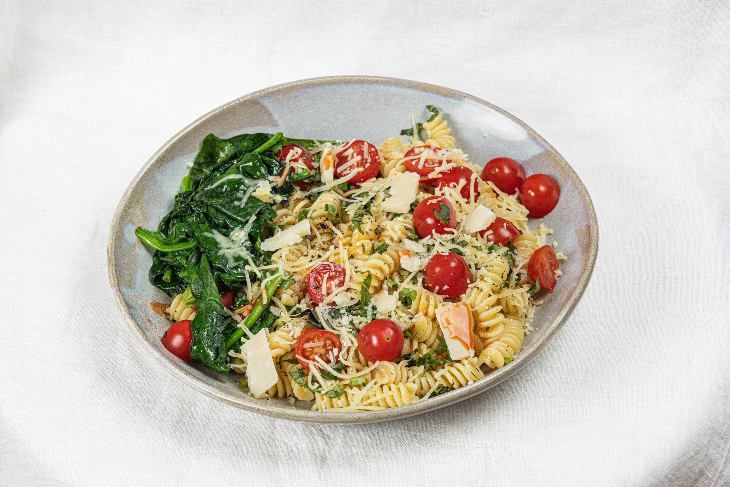 Salade de pâtes avec tomates cerises, épinards et fromage râpé dans une assiette. Par le photographe culinaire Yves Daniel. 