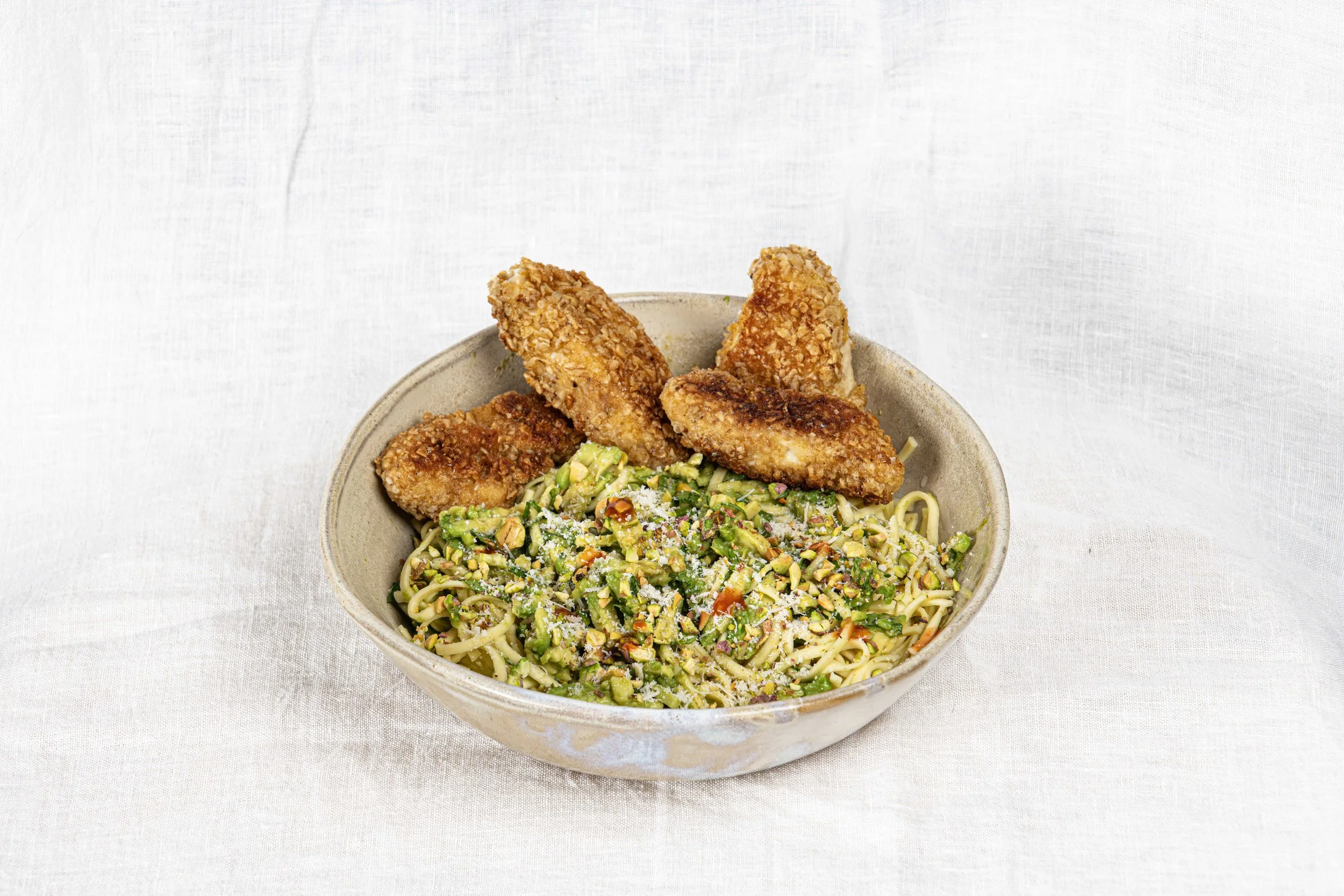 Bol de pâtes avec des légumes hachés, parsemés de parmesan, accompagné de morceaux de poulet pané et frit. Par le photographe culinaire Yves Daniel. 