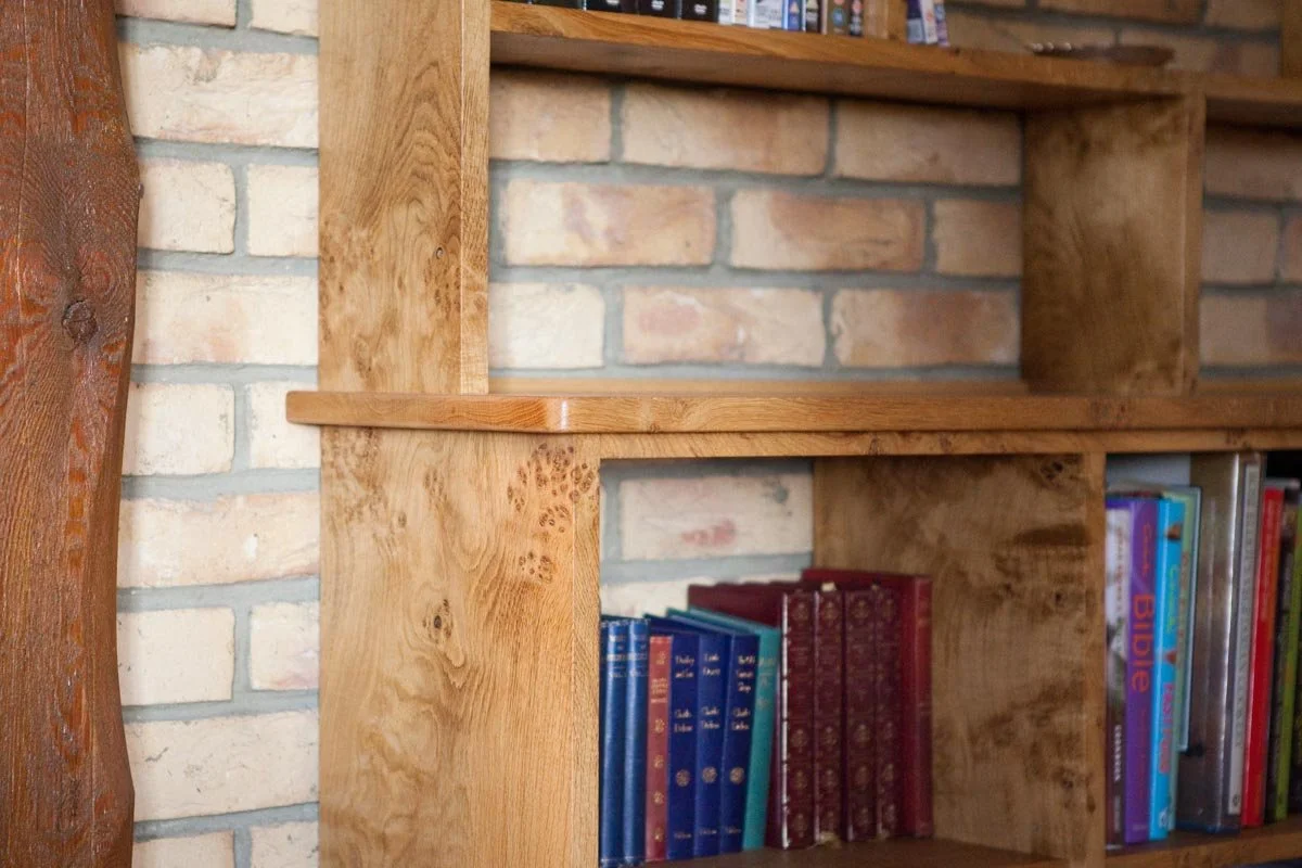 Close-up of a wooden bookshelf against a brick wall, with colorful books visible on the shelves.