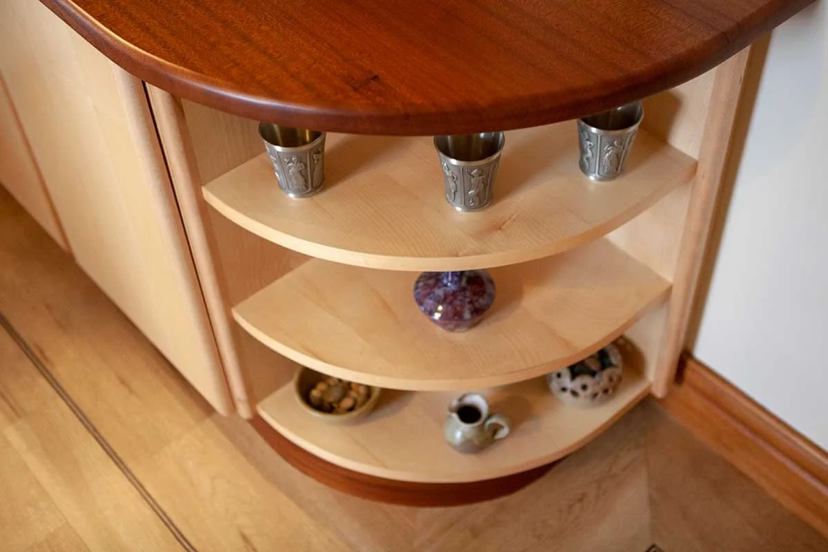 Corner wooden shelf unit with five shelves holding various decorative items and metal cups.