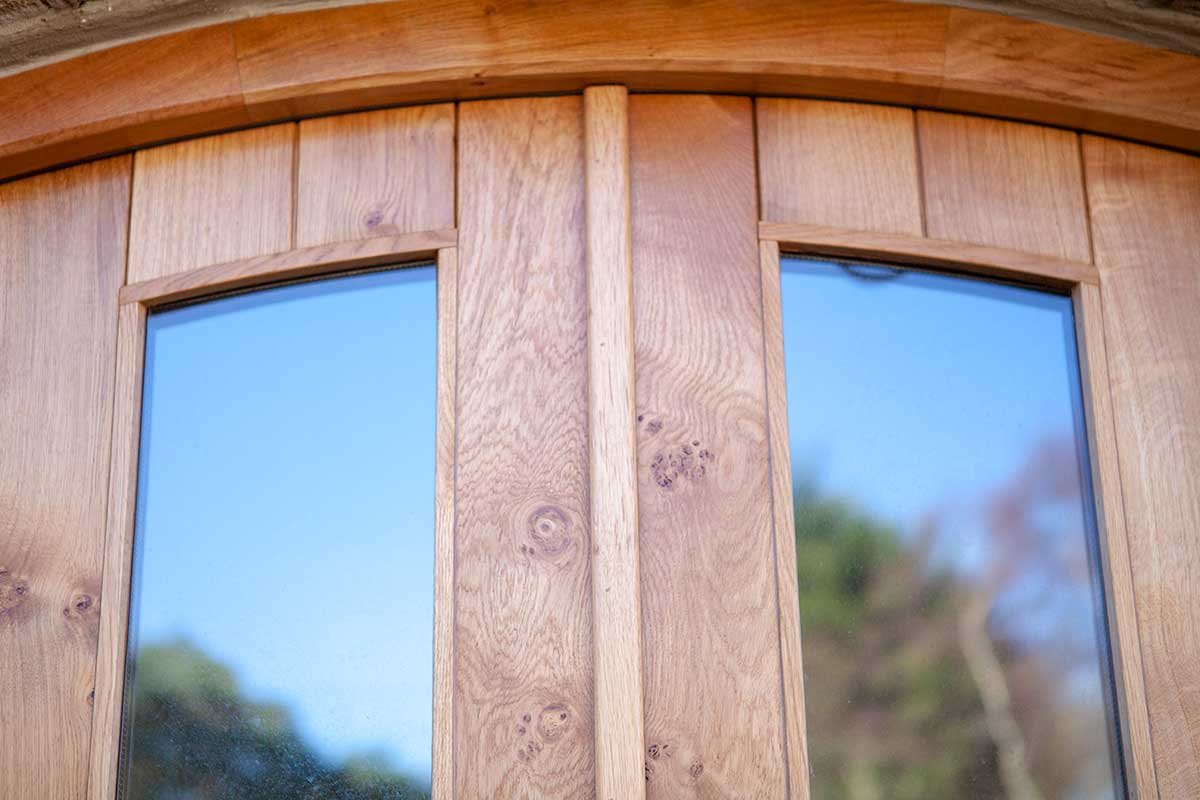 Close-up of a wooden window frame with two glass panes reflecting the blue sky and trees outside.