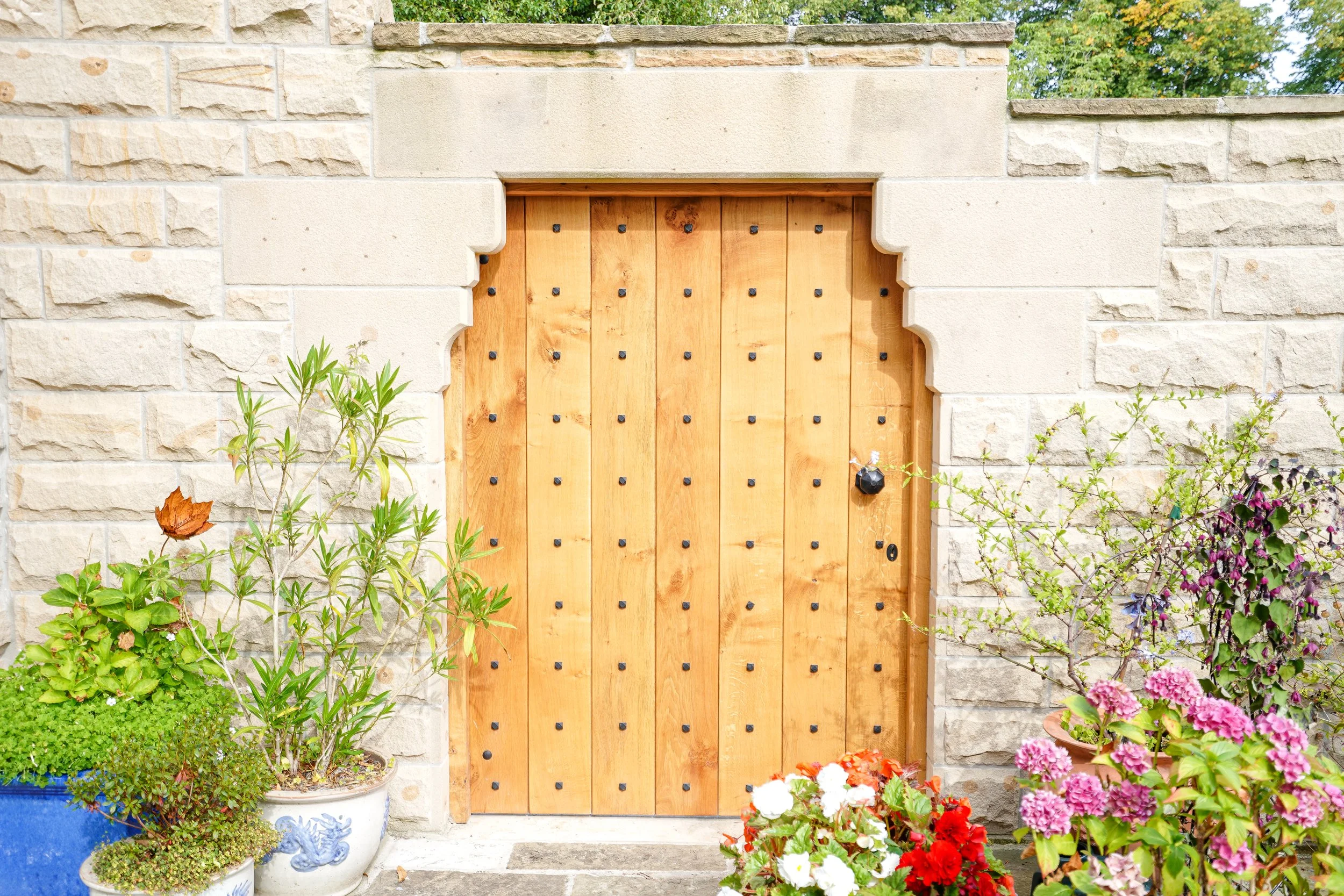 Wooden door set in stone wall with potted plants and flowers outside.