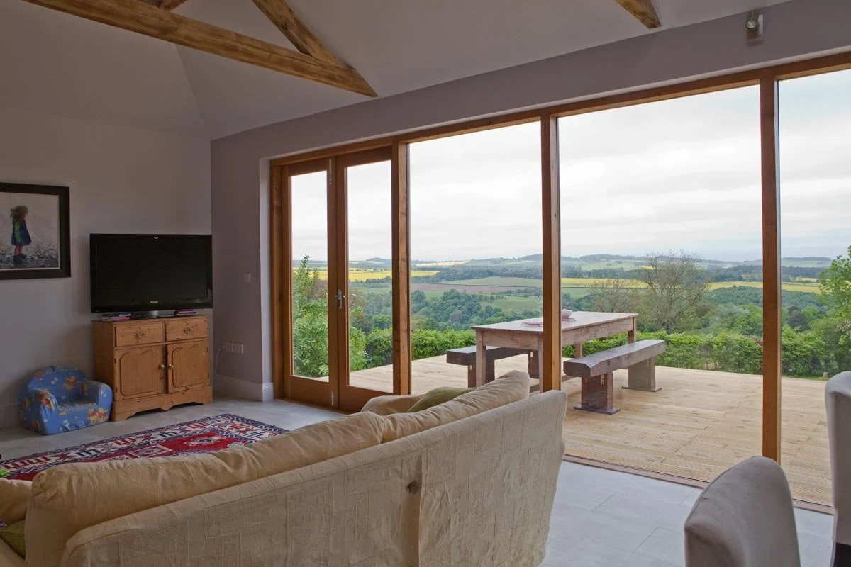 Living room with large glass sliding doors opening to a wooden deck with a view of rolling hills and countryside.