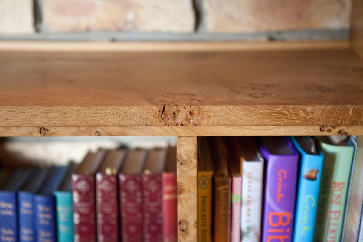 Close-up of a wooden bookshelf with blurred colorful books underneath.