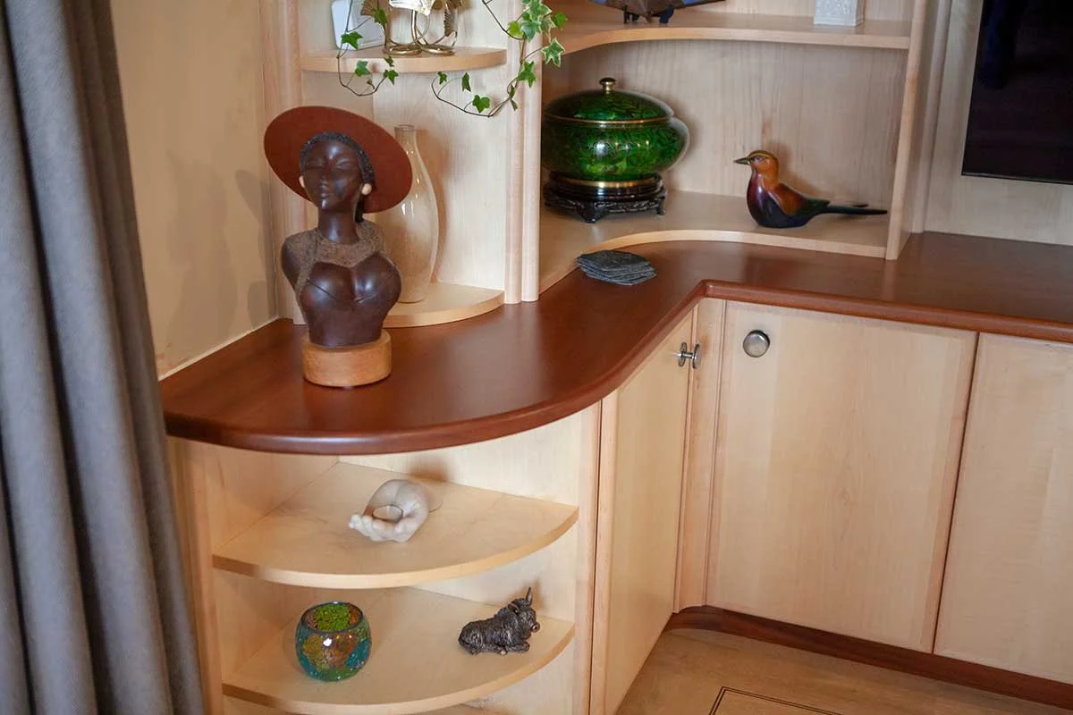 Decorative wooden cabinet with sculptures, vases, and decorative objects, including a bust of a woman, a ceramic bird, and a colorful glass bowl.