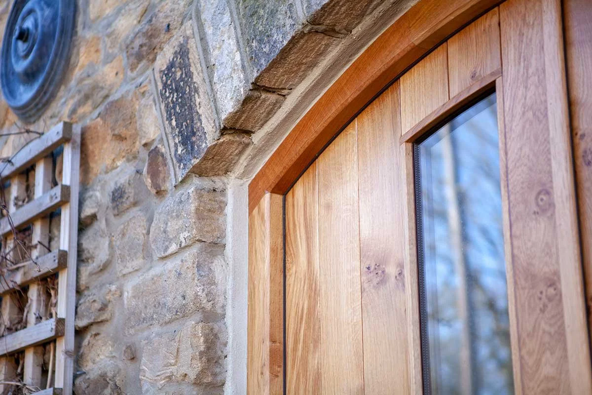 Close-up of a wooden door with a glass panel, set in a stone wall with a stone arch.