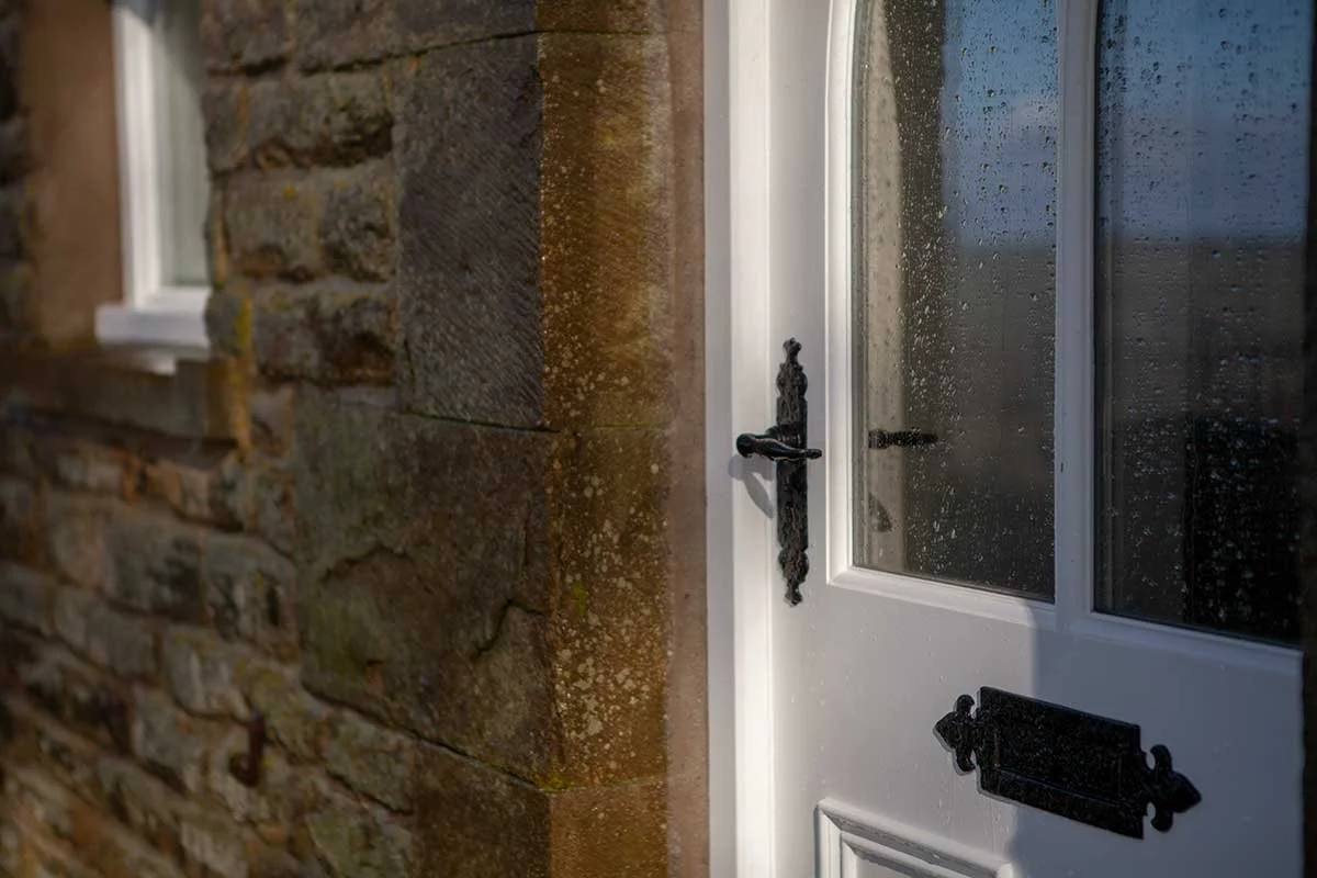 Close-up of a white and glass door we made for a property in northumberland, with stone walls. The door has a black handle and a black letterbox.