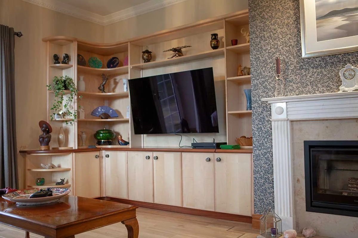 Living room with a built-in wooden entertainment center, a large flat-screen TV, decorative items, a fireplace with a mantle, and a coffee table with a decorative tray.