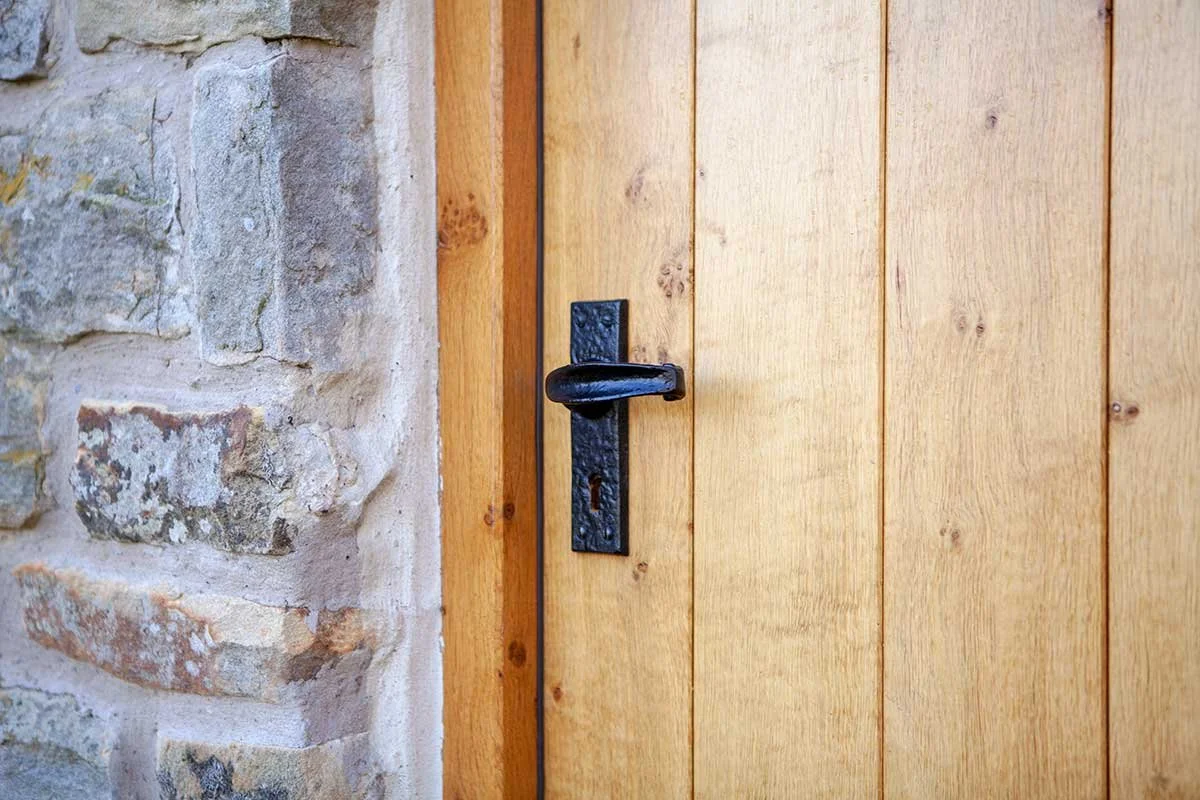 A wooden door with a black iron handle and keyhole, set next to a stone wall.