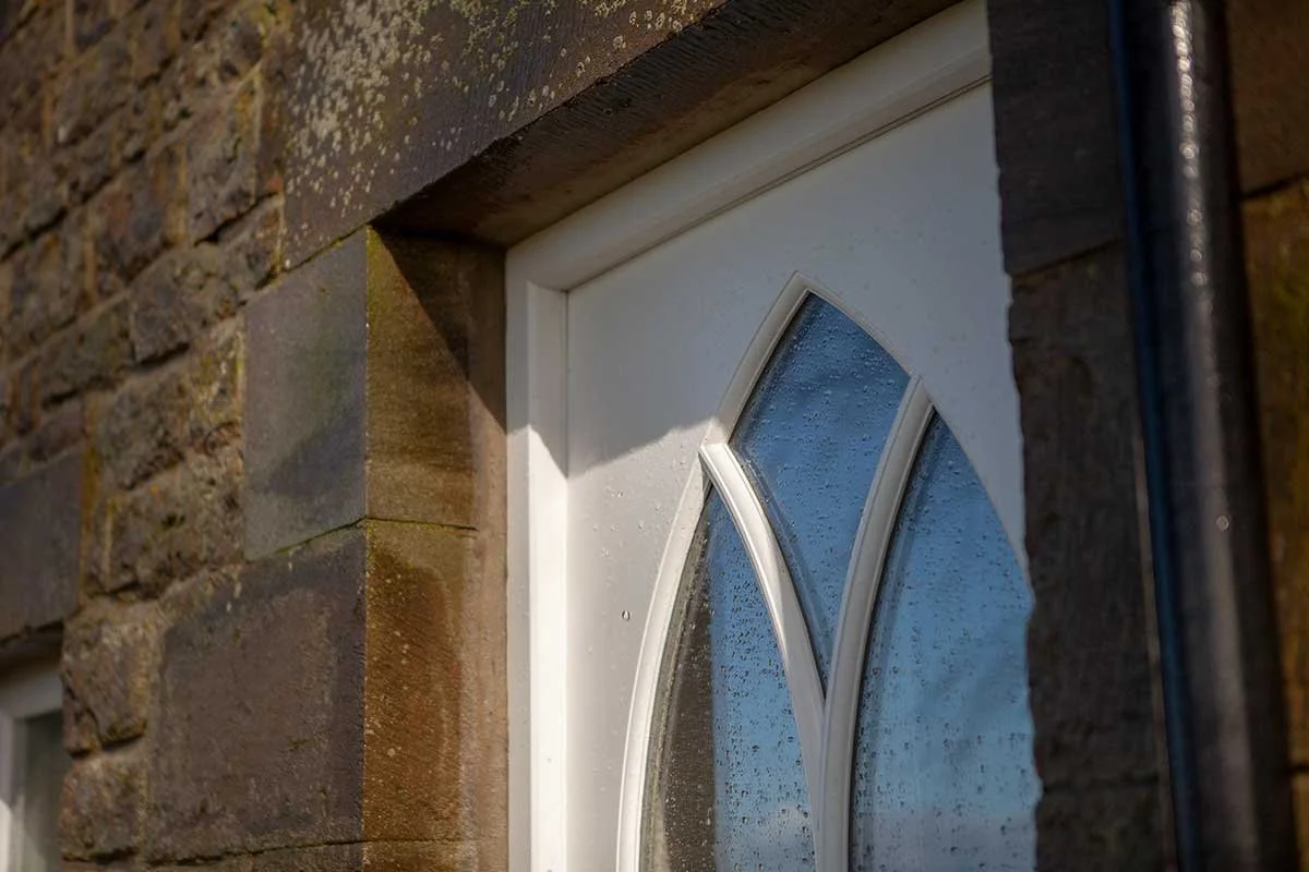 Close-up of a white front door we made, with glass panels, surrounded by stone walls, showing craftsmanship and exterior detailing.