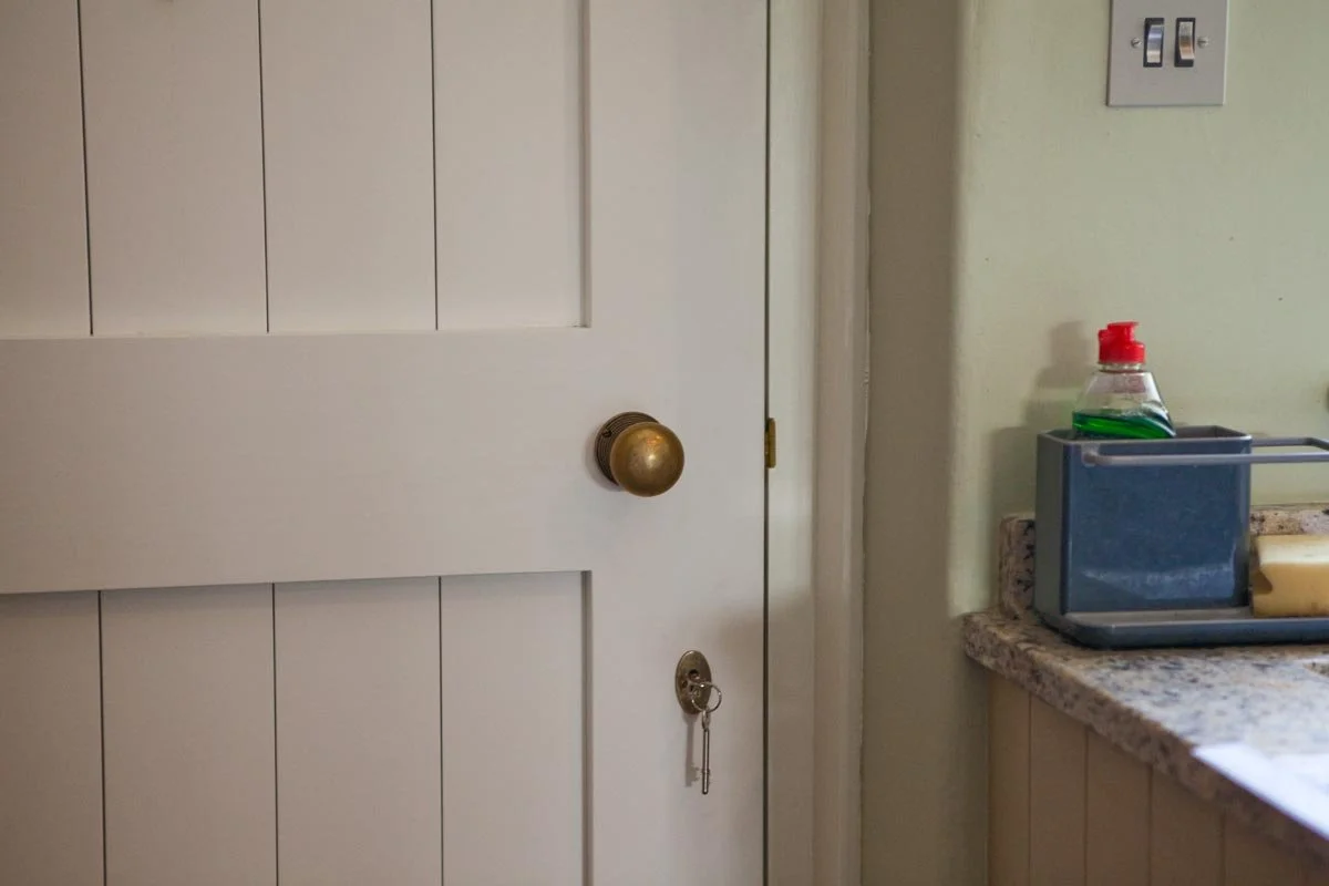 Part of a kitchen with a white door, a brass doorknob, and a key hanging from a keyhole. There's a granite countertop with a blue bread box, a dish soap bottle, and a bar of soap on a soap dish.