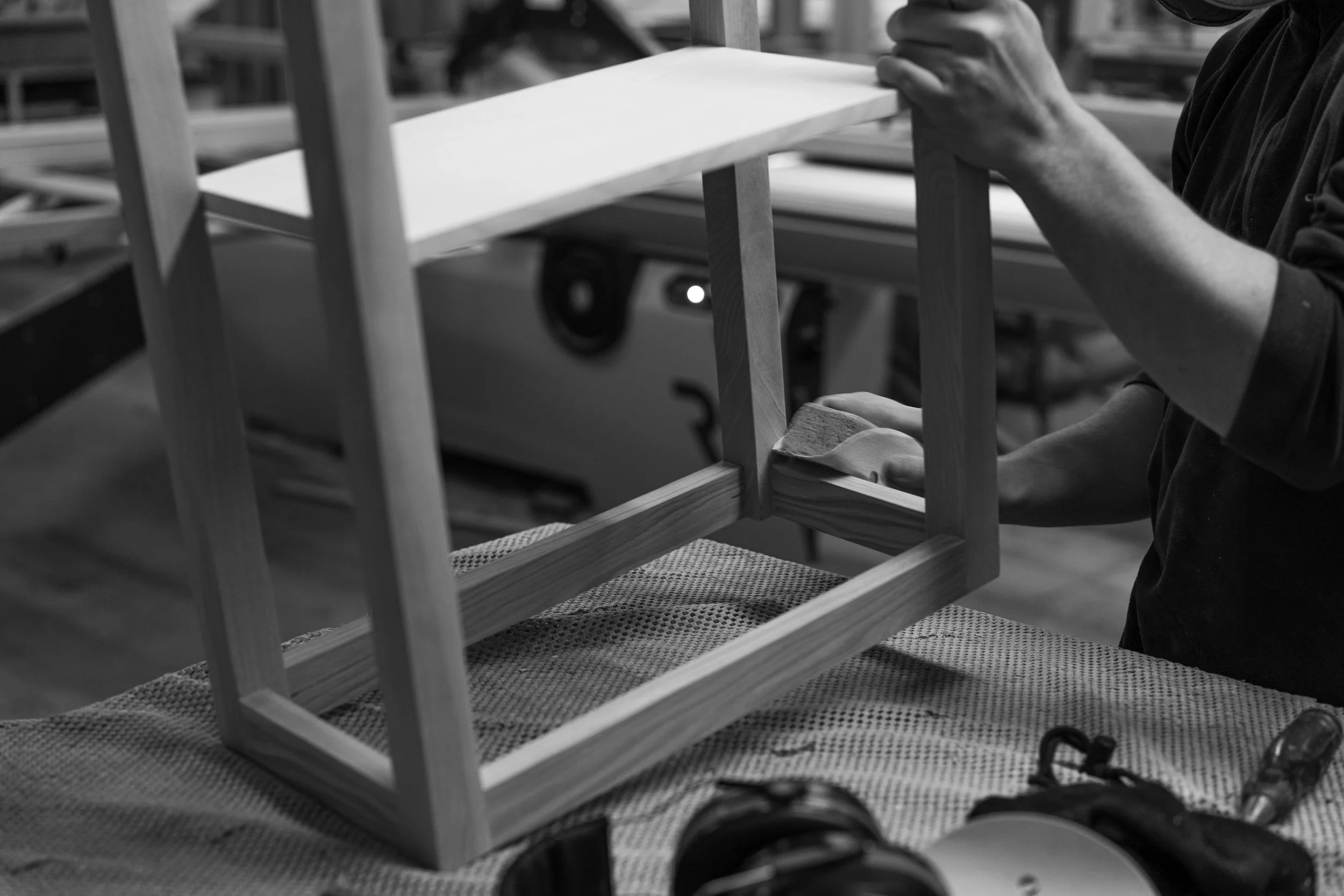 Person smoothing wood with a sanding block while constructing a small wooden frame in a woodworking shop.