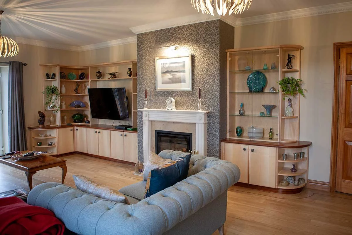 Living room with a gray tufted sofa, wooden cabinets, a fireplace, a wall-mounted TV, and open shelves with decorative items.