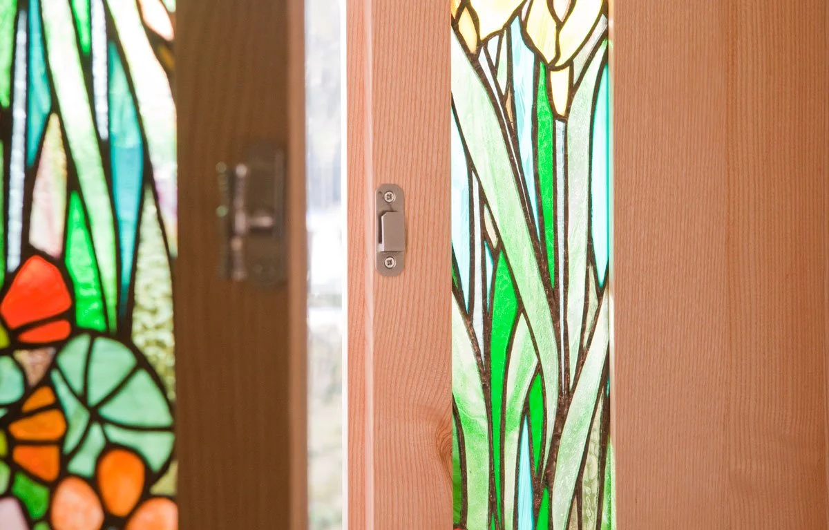 Close-up of stained glass door with a floral and leaf pattern, framed by wooden edges.