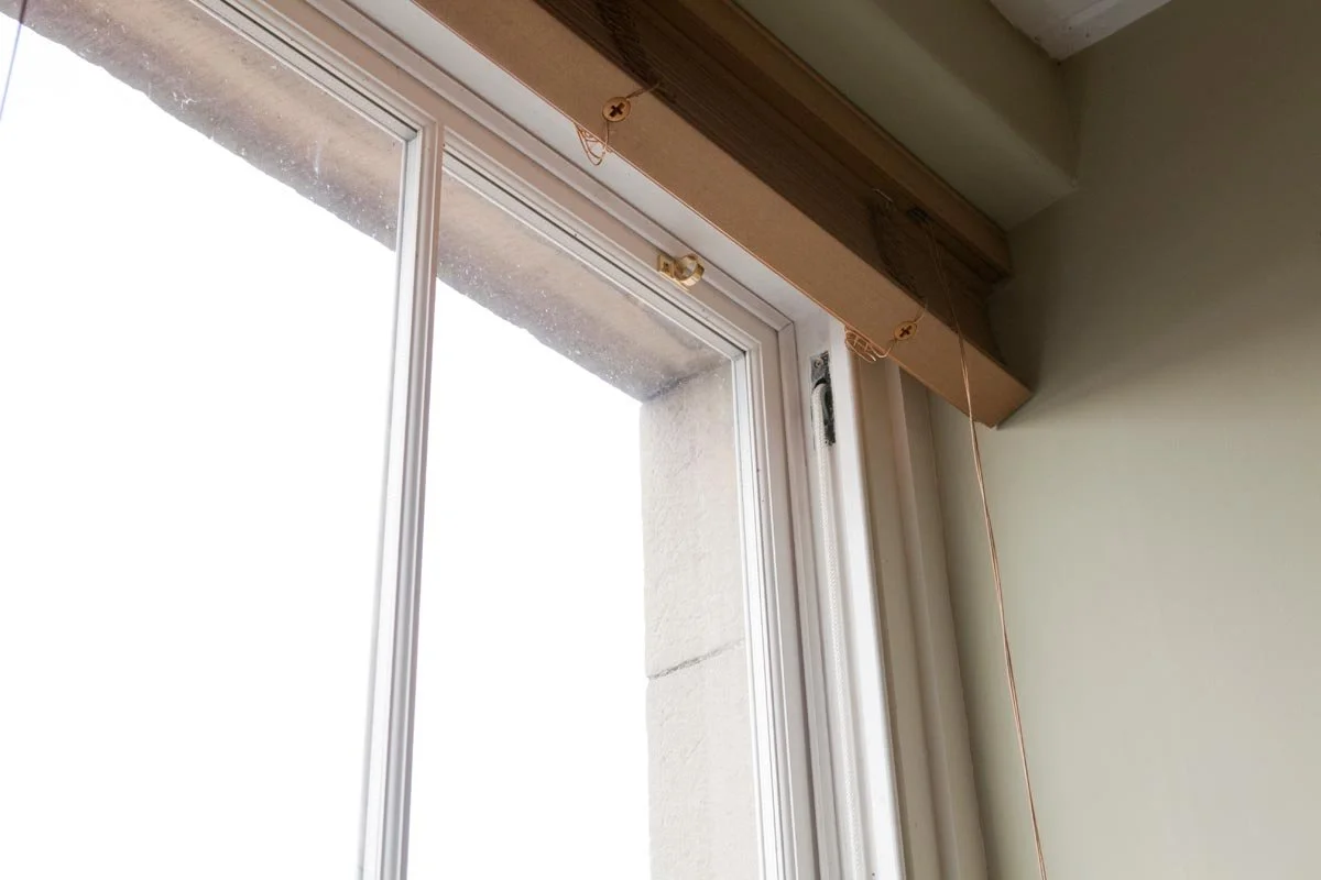 Close-up view of a window with a partially installed window valance or curtain rod, showing hooks and hardware underneath the wooden trim.