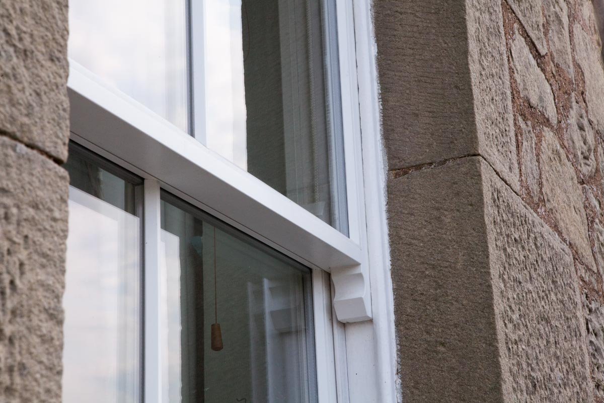 Close-up of a residential window with white framing, set into a textured brick and stone exterior wall.