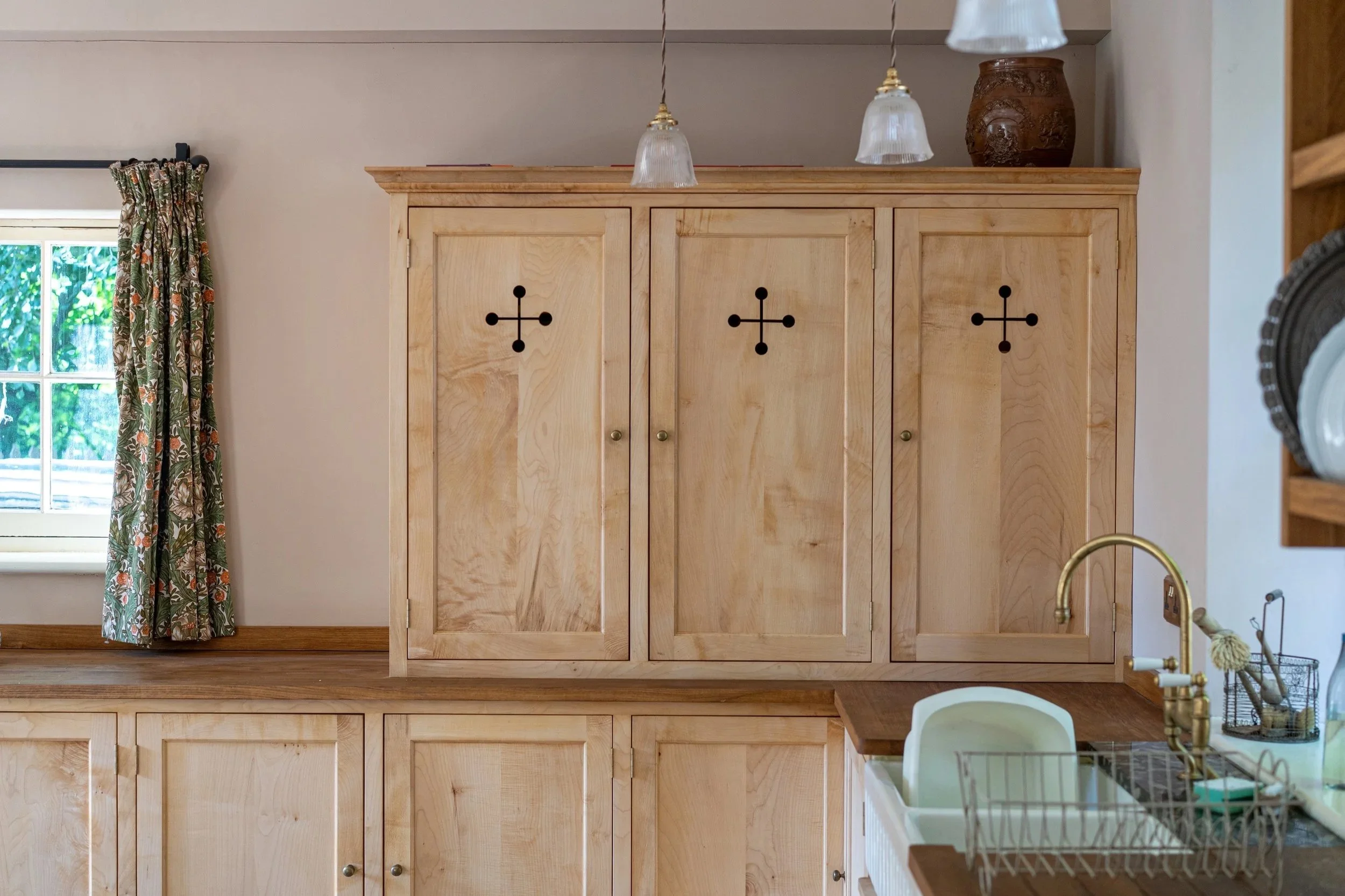 Kitchen with light wood cabinets, a window with floral curtains, and a gold faucet in the sink.