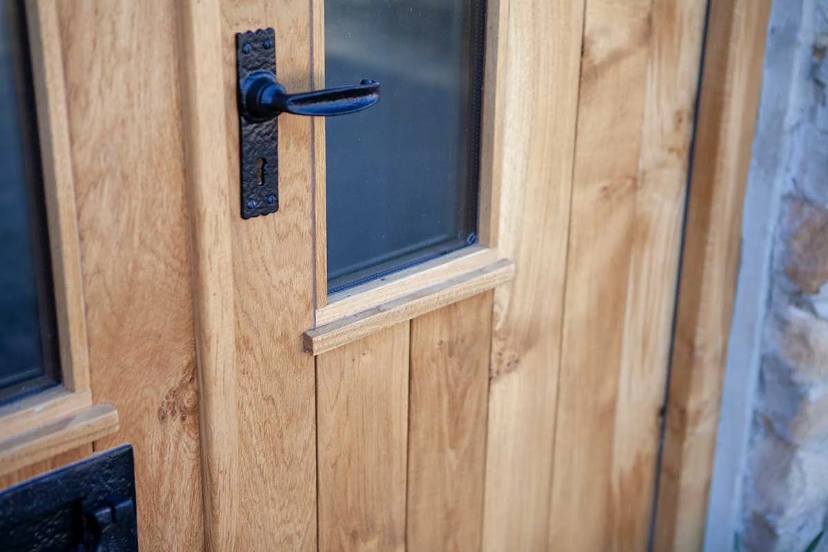 Close-up of a wooden door with a black metal handle and a small window with a wooden frame.