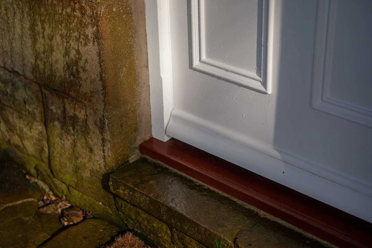 Close-up of a white front door with a wooden door sill, set in a traditional stone property.