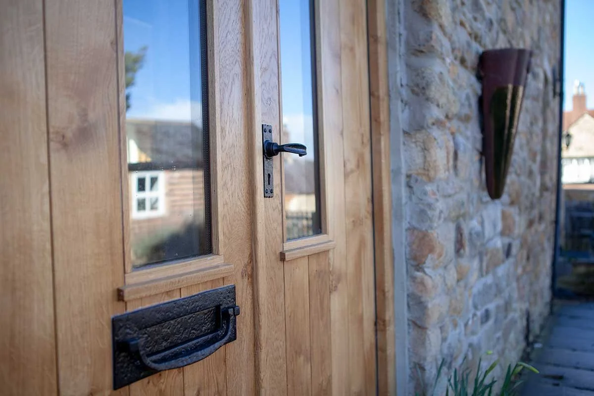 Close-up of a wooden door with a black handle and a small glass window, next to a stone wall with a wall-mounted decorative piece.
