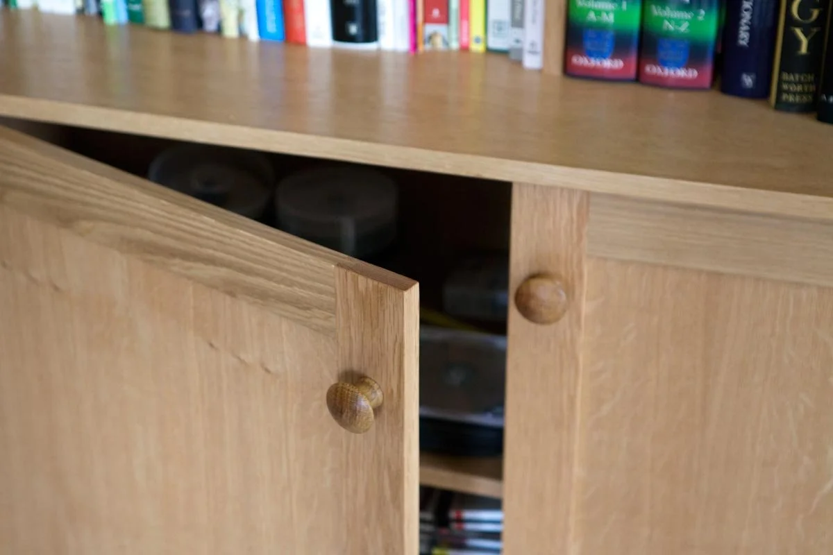 A wooden bookshelf with books on top and a partially open cabinet door revealing storage inside.