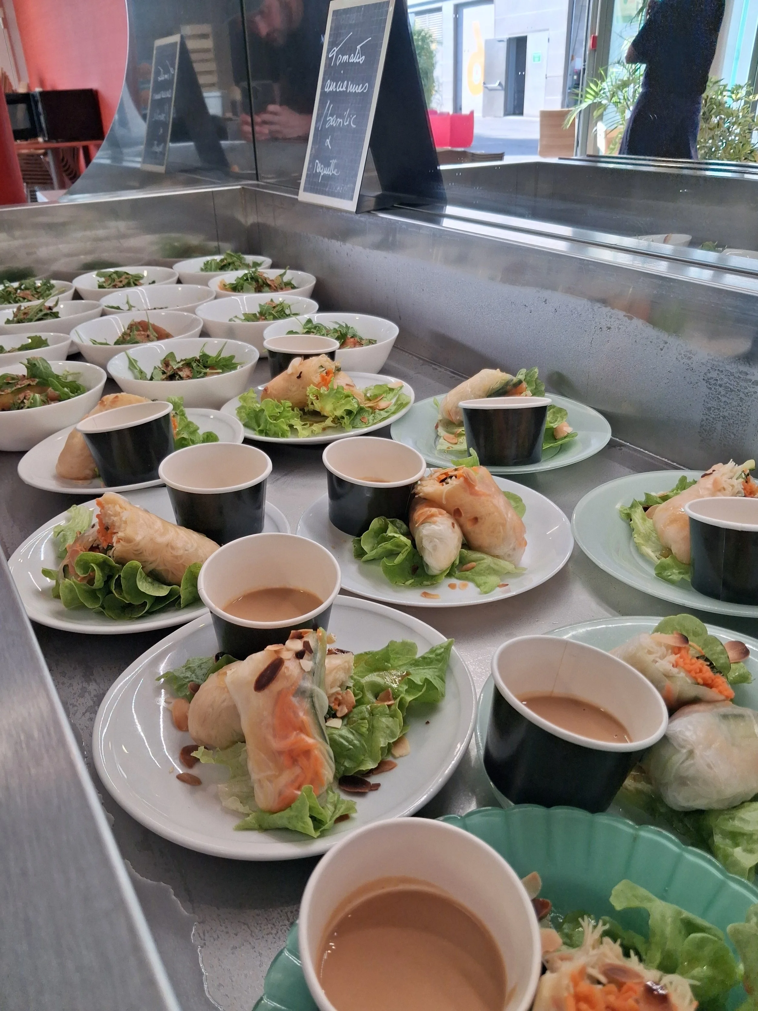 Assortiment de plats à base de rouleaux de printemps, salades, et soupes dans une vitrine de restaurant.