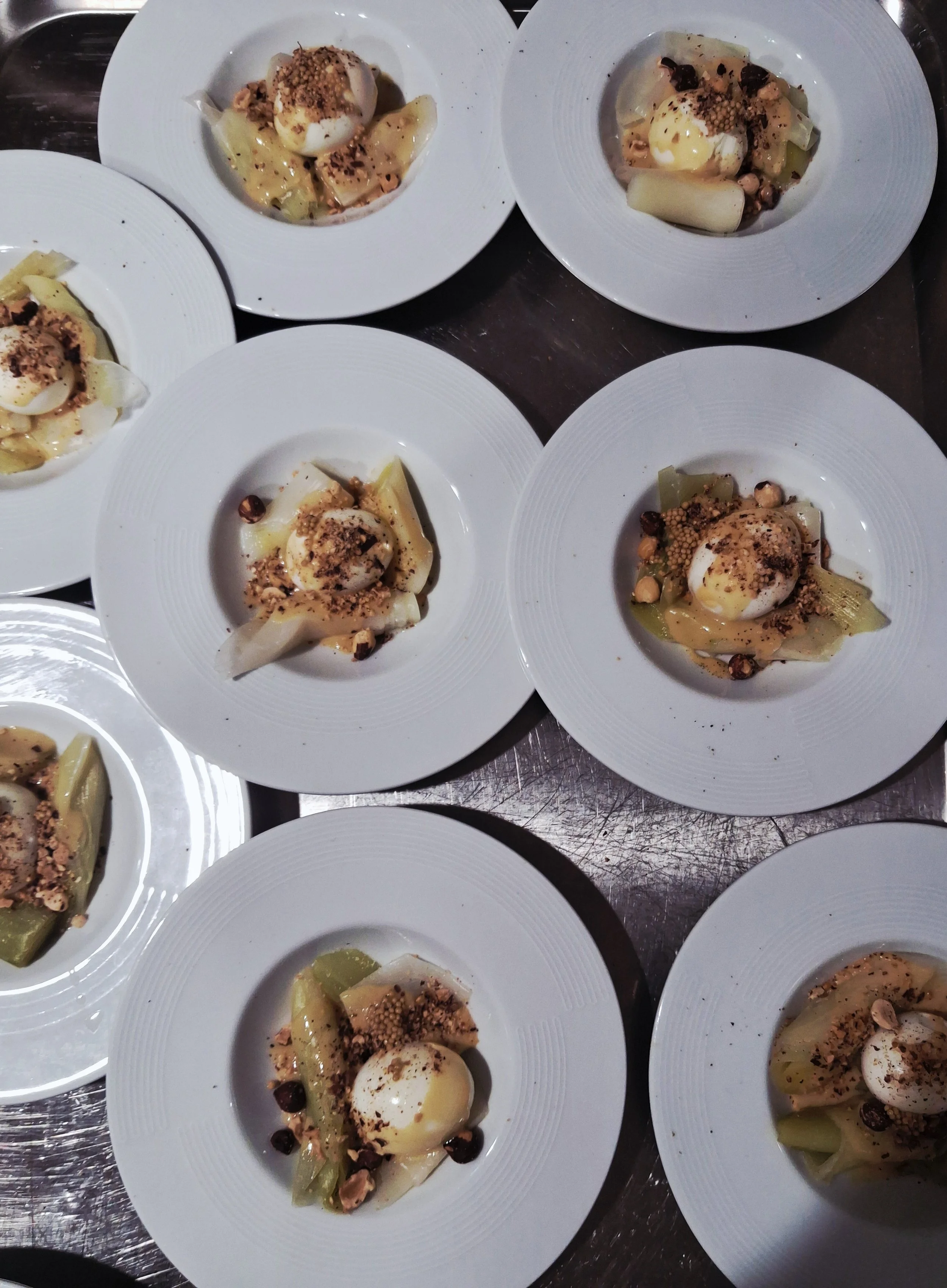 Plats de huevos pochés servis avec une sauce, des légumes, des noisettes et des graines.