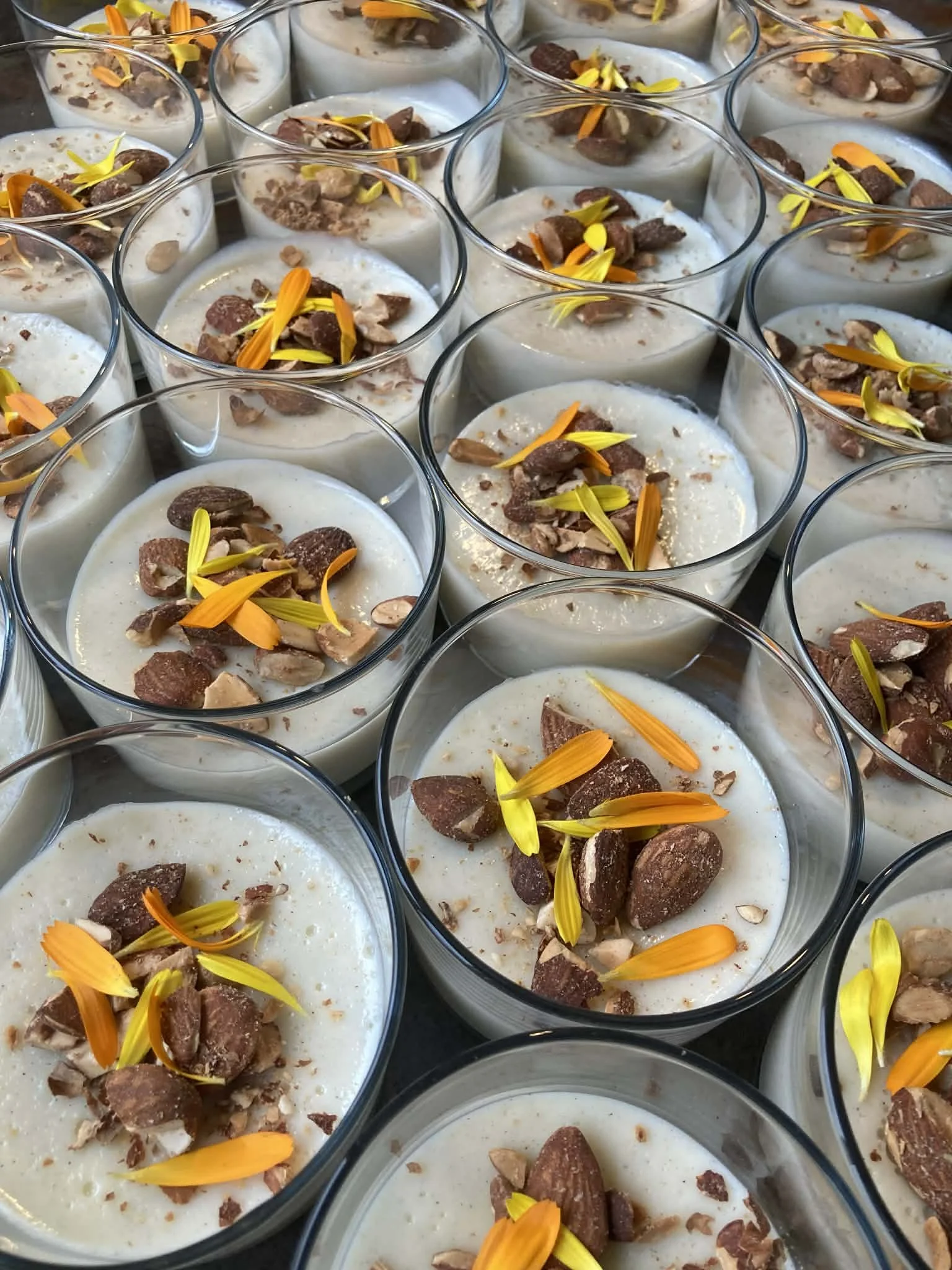 Desserts en verrines garnis de morceaux de chocolat, de noix et de fleurs comestibles colorées.