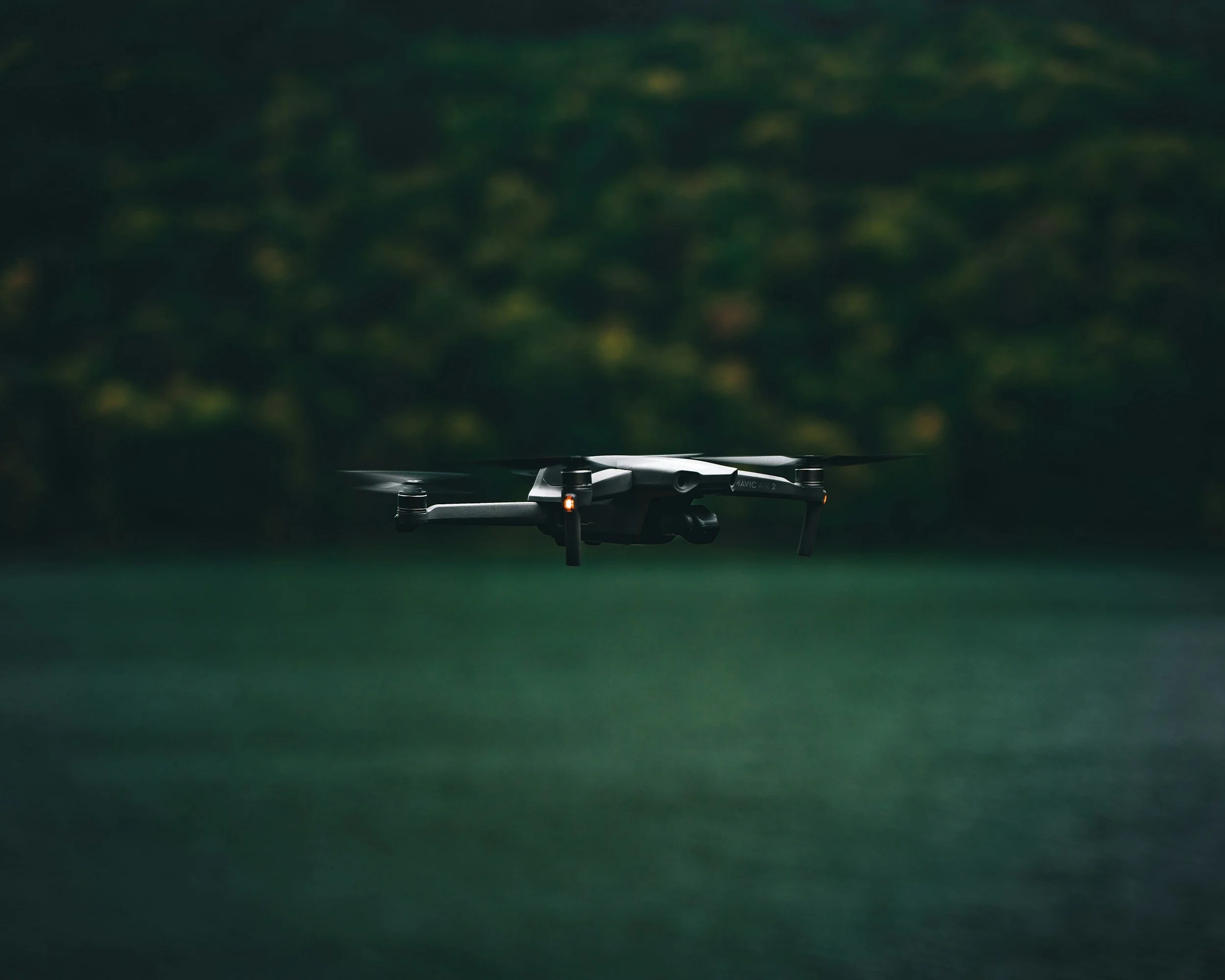 Un drone en vol au-dessus d'une surface verte avec un arrière-plan flou de feuillage