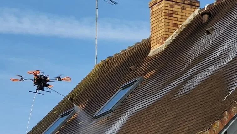 Drone pulvérisant un produit sur le toit d'une maison avec des fenêtres de toit.