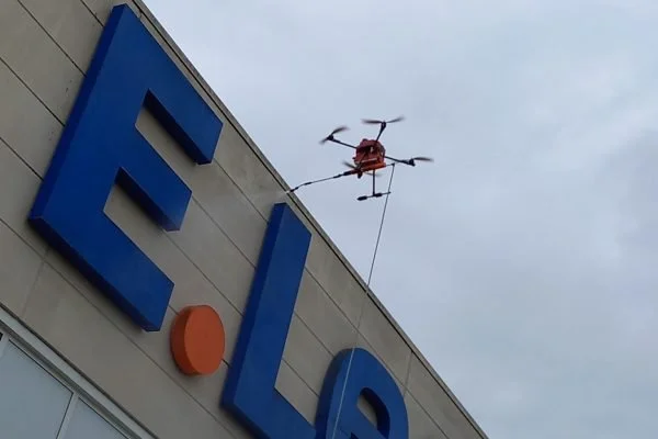 Un drone suspendu par une corde au-dessus d'une façade avec des lettres bleues et orange.