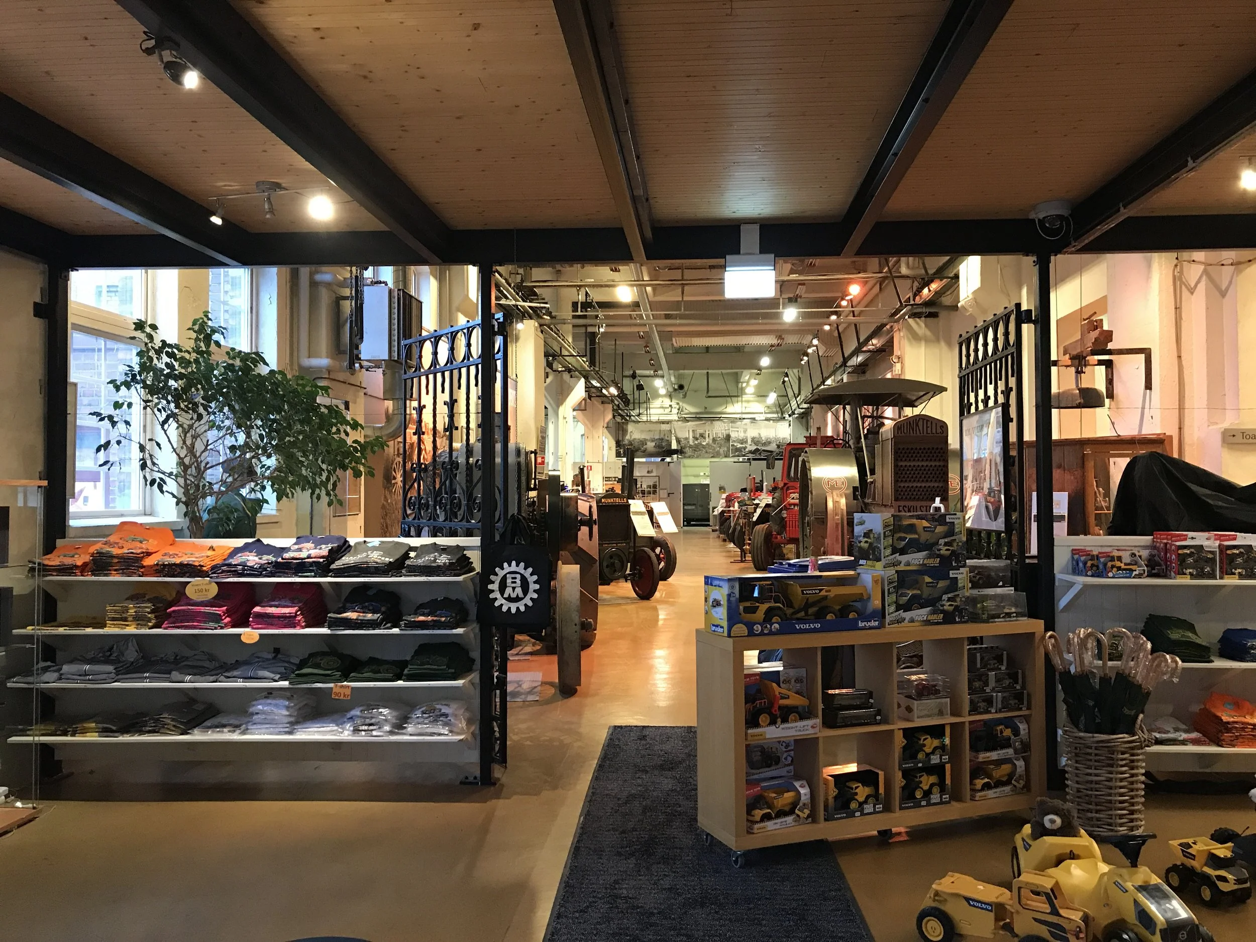 View of a toy store with shelves displaying toy cars, remote control cars, and clothing, along with vintage tractors in the background.
