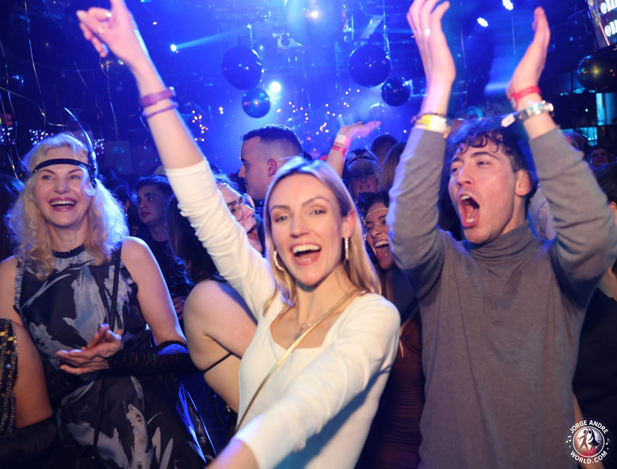 People dancing and enjoying at a nightclub with colorful lights and disco balls overhead.