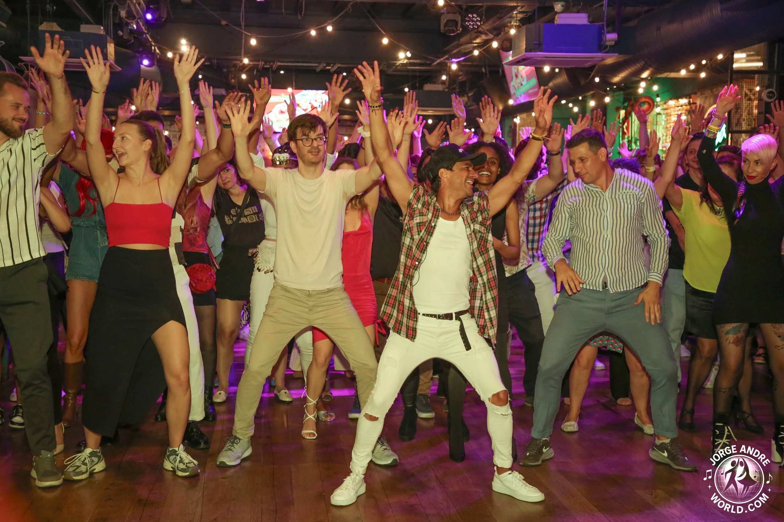 A group of people dancing and having fun at a party or dance event with colorful lights and decorations in the background.