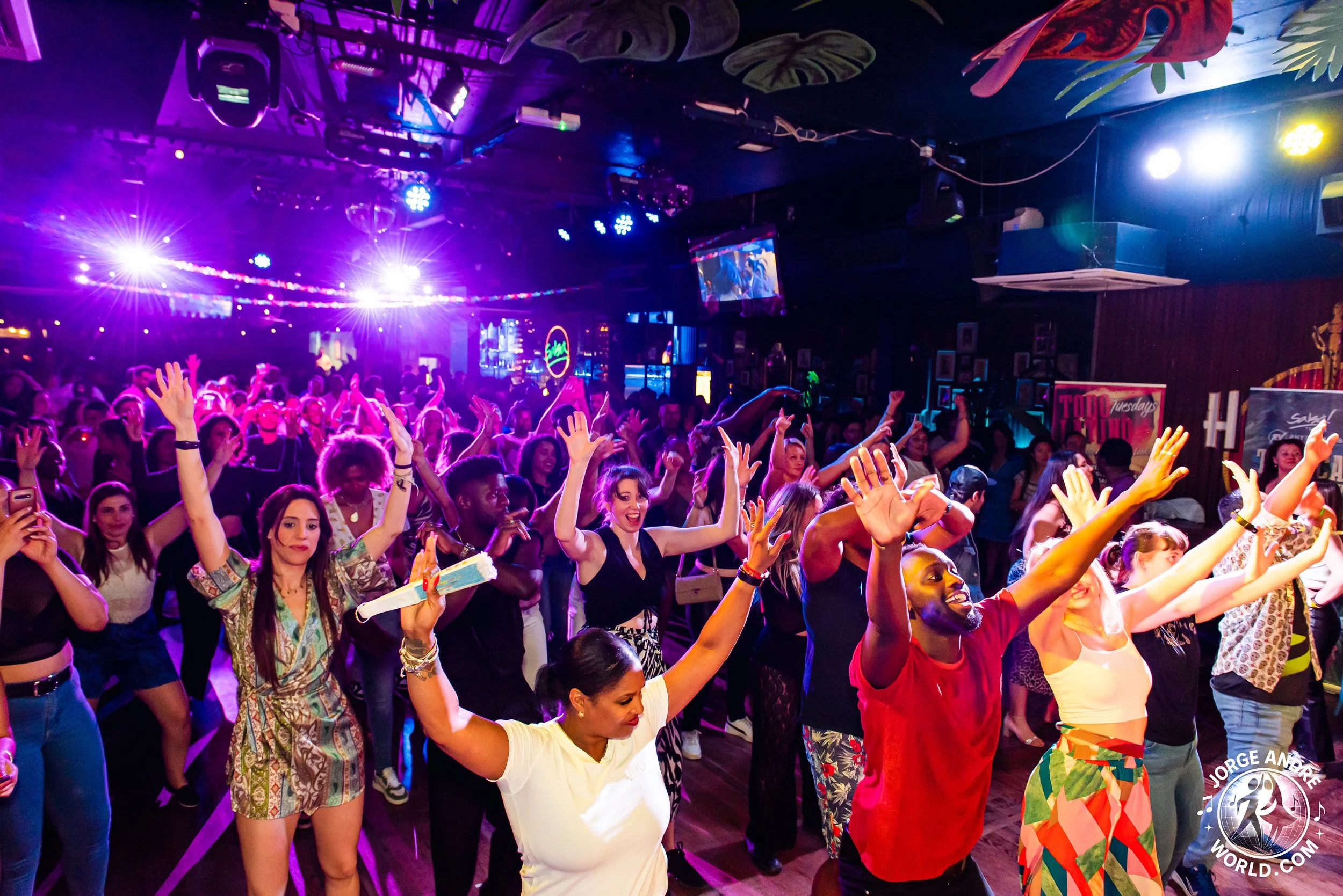 People dancing and enjoying live music in a vibrant nightclub with colorful lighting and decorations.