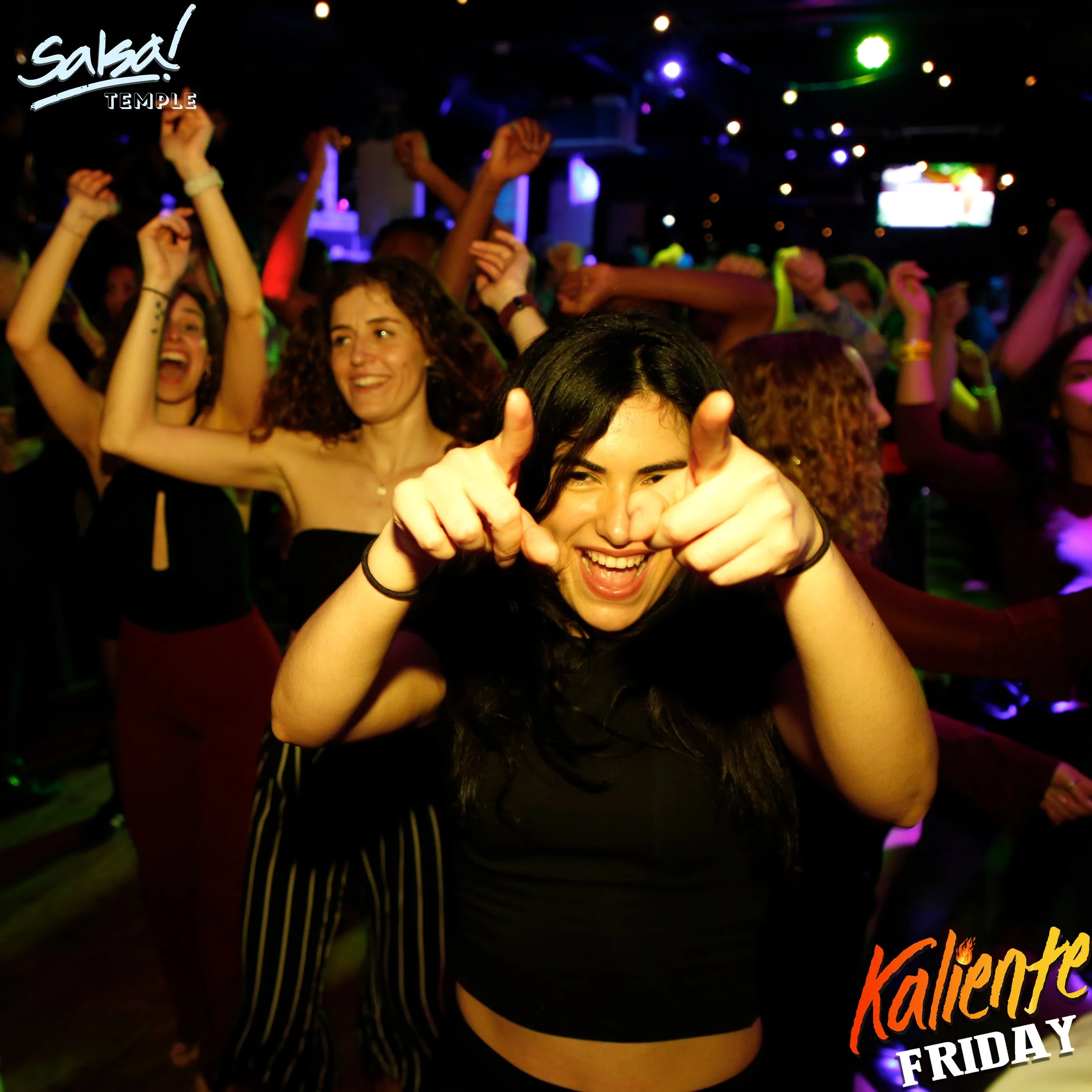 Group of young women dancing and having fun at a party or nightclub with colorful lights and a lively atmosphere.