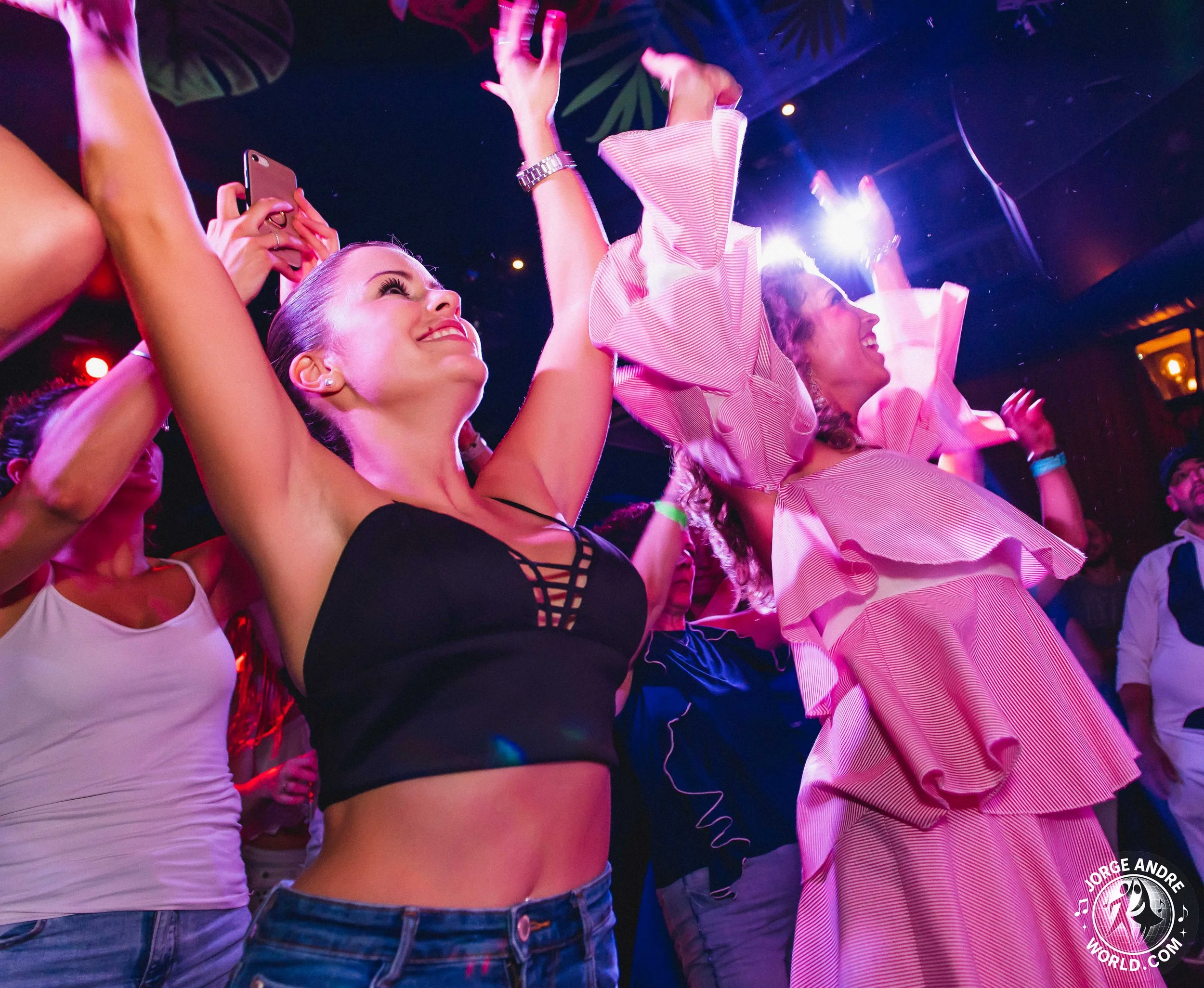 People dancing and enjoying music at a lively concert or club, illuminated by colorful stage lights.