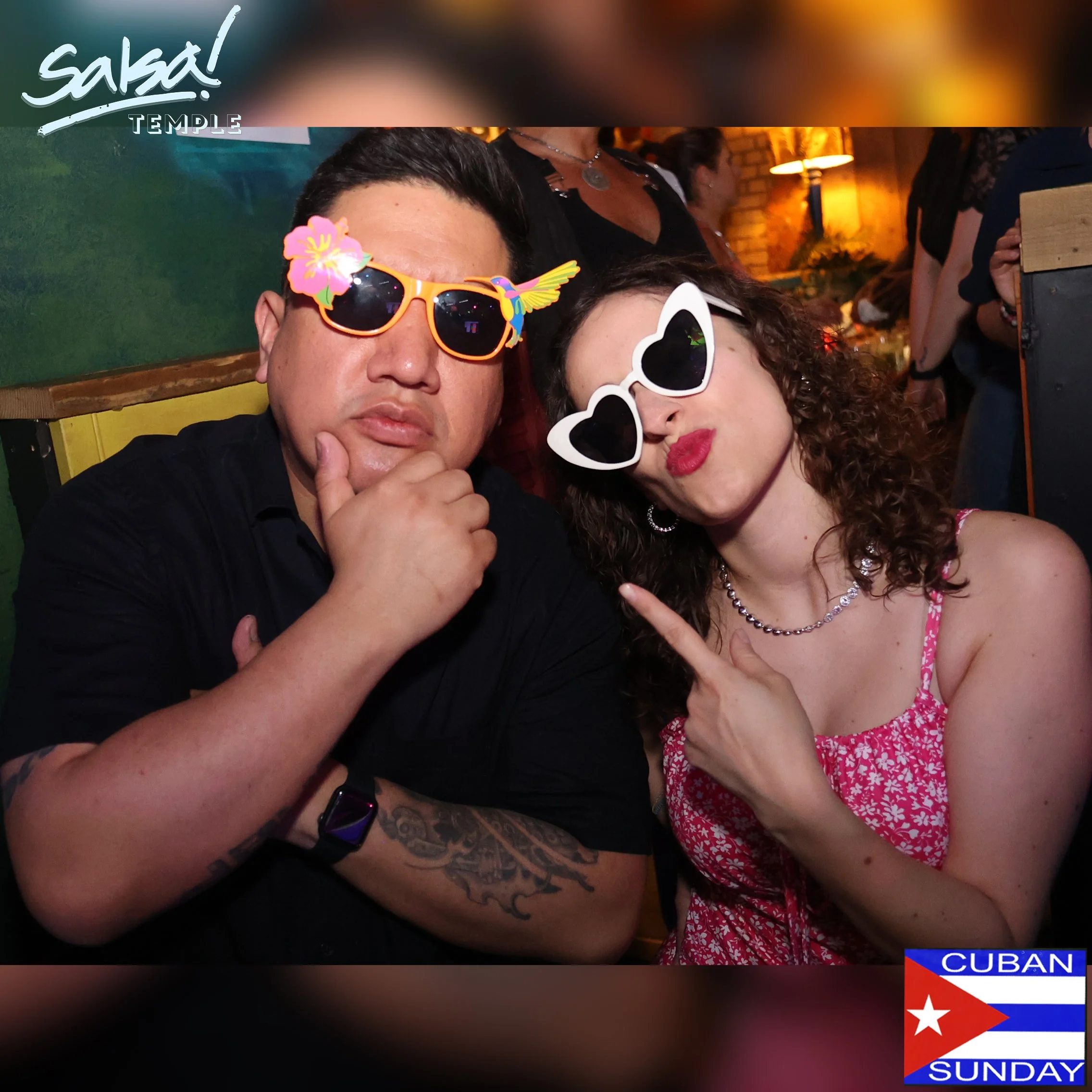 Two people at a Salsa event, wearing colorful sunglasses and making playful gestures, with a Cuban flag and the words 'Cuban Sunday' in the corner.