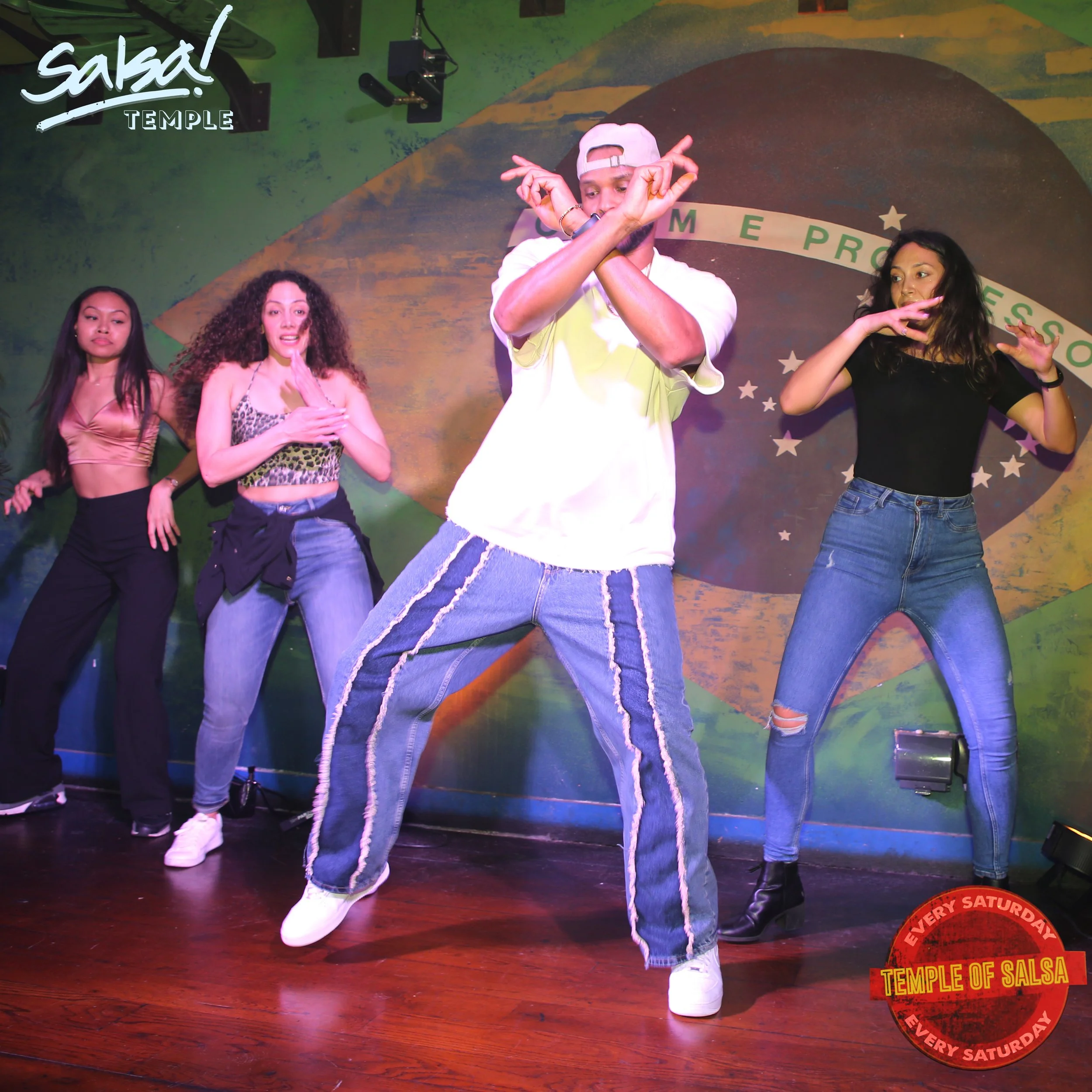 Group of people dancing on stage at a salsa event, with a green and yellow background resembling the Brazilian flag, and a logo in the top left corner that says 'salsa! TEMPLE'.