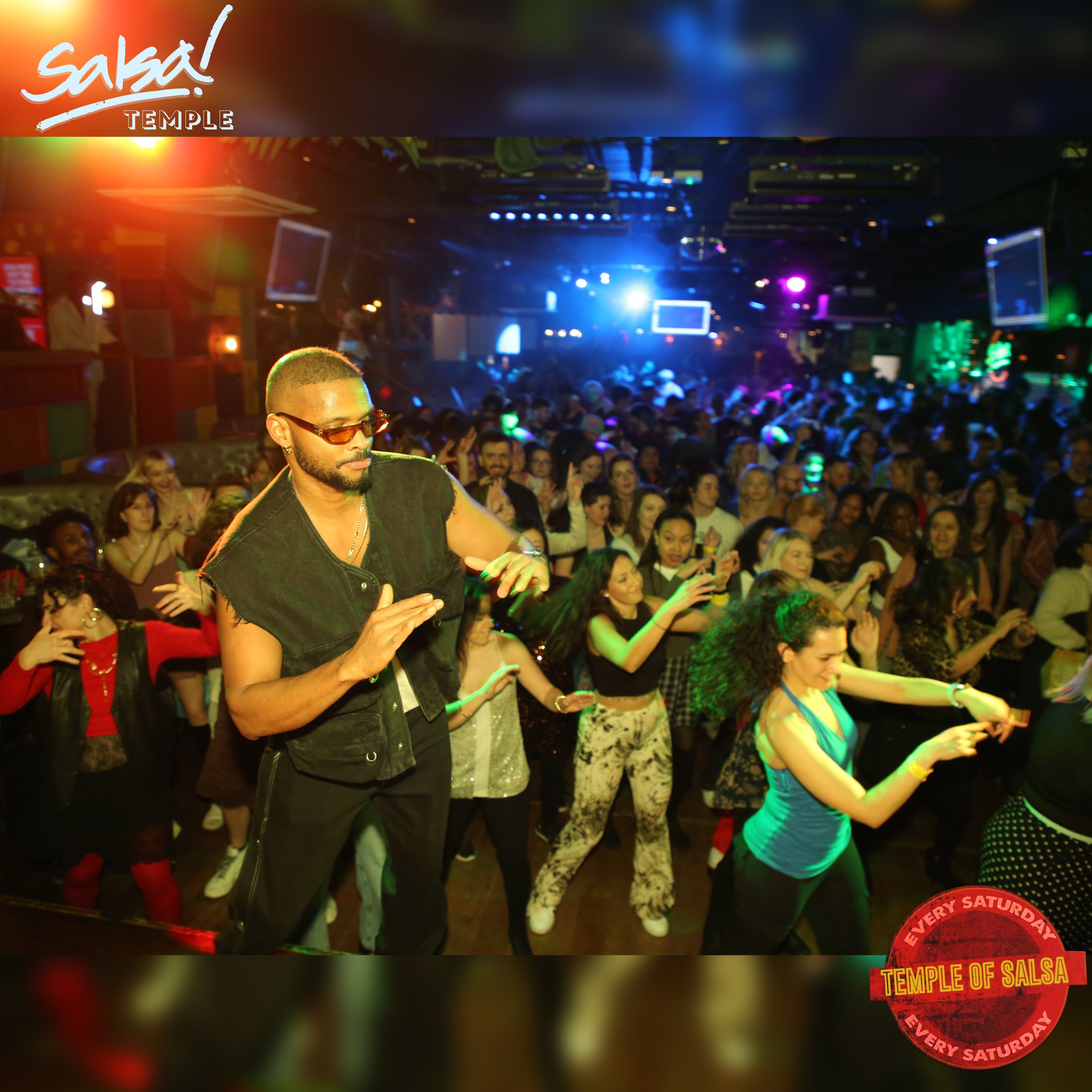 A lively dance event at a salsa club featuring diverse people dancing in a colorful, illuminated venue with a DJ and stage lights, advertising 'Salsa Temple' every Saturday.