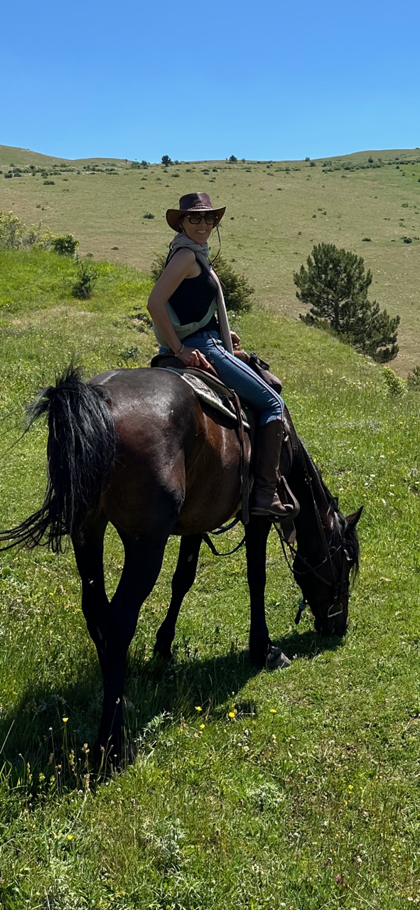 Une femme à cheval dans un paysage montagneux verdoyant ensoleillé.