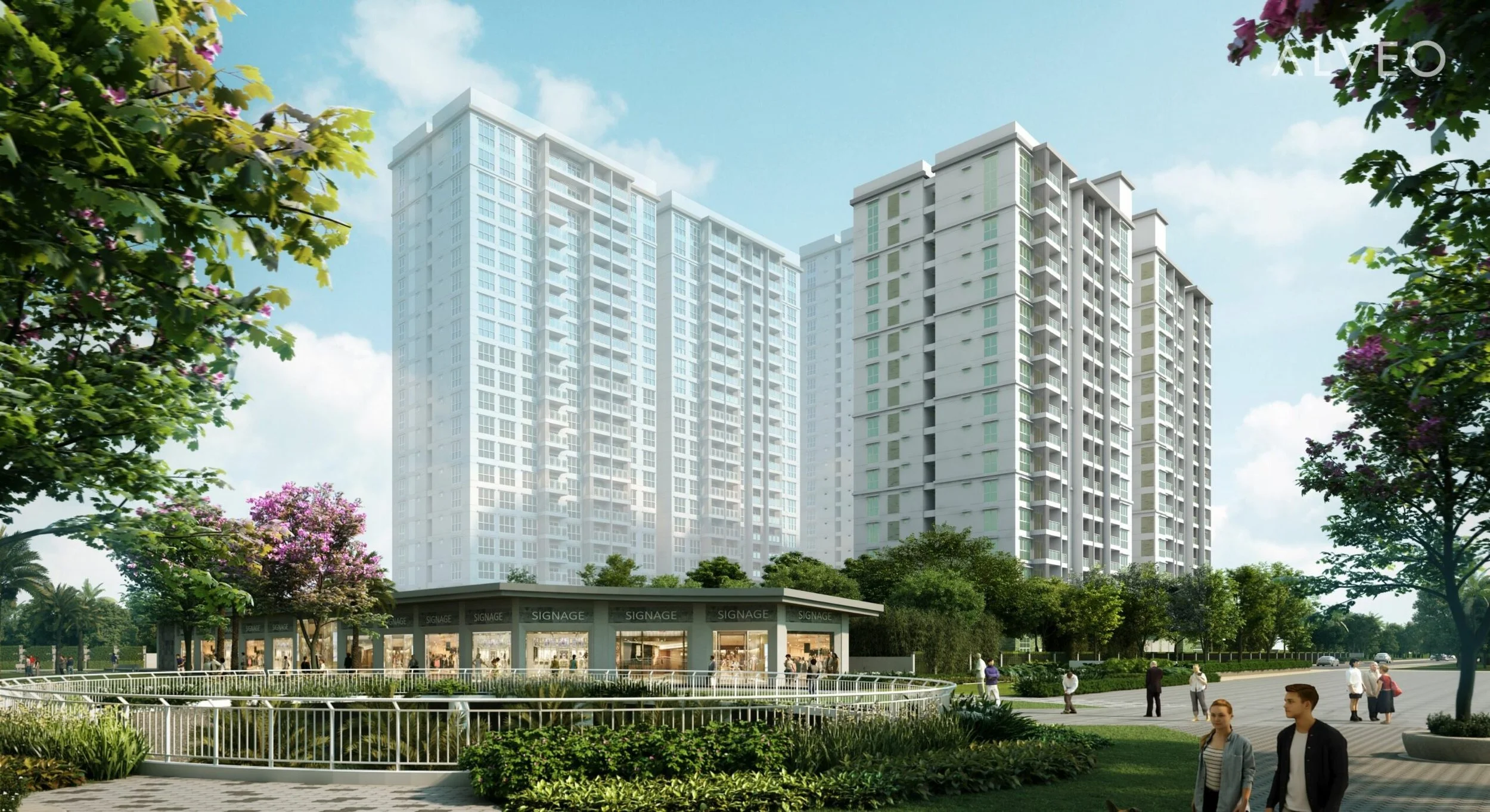 Modern residential complex with tall high-rise buildings, landscaped gardens, a commercial space with signage, and people walking outdoors on a sunny day.