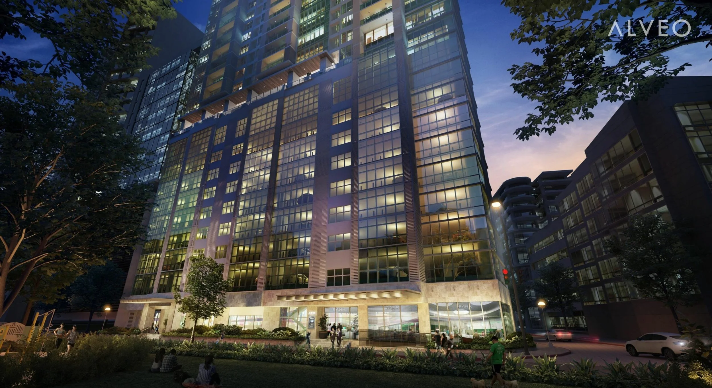 Nighttime view of a modern high-rise building with glass windows, illuminated inside, in an urban setting. People are walking and sitting in a park area with trees and streetlights in the foreground.