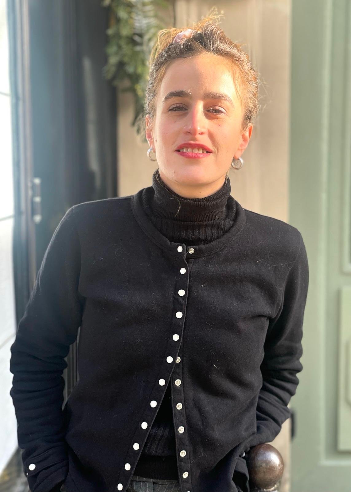 Portrait en noir et blanc d'une femme avec des cheveux bouclés et un regard intense, posant devant un mur en pierre.