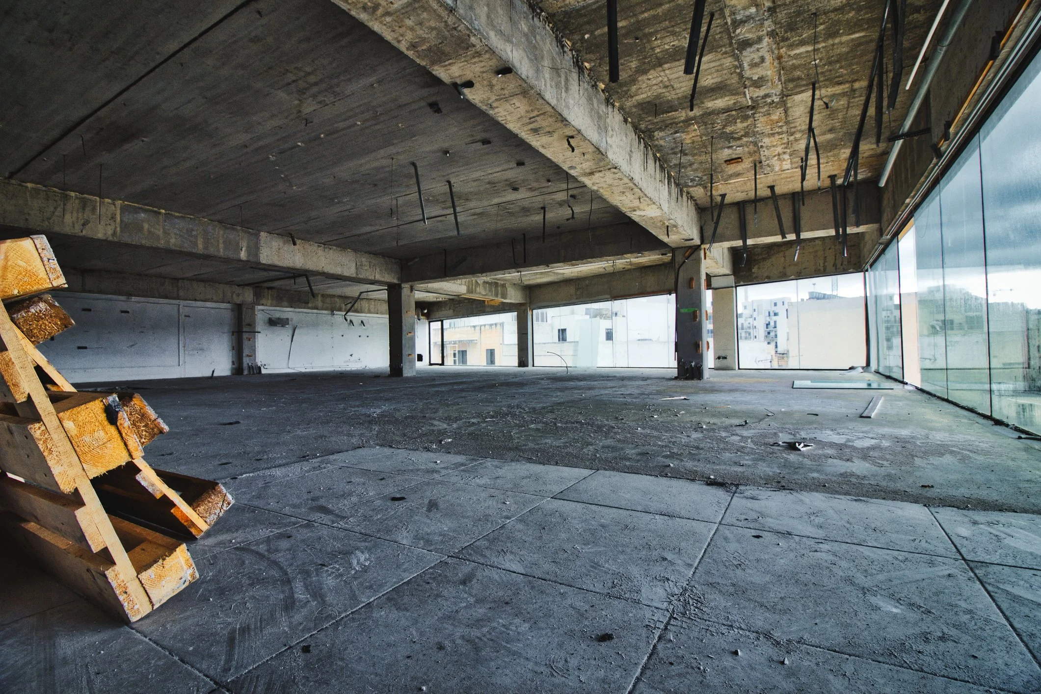 Interior of an unfinished building under construction with exposed concrete floors, ceilings, and support columns, and large windows providing natural light.