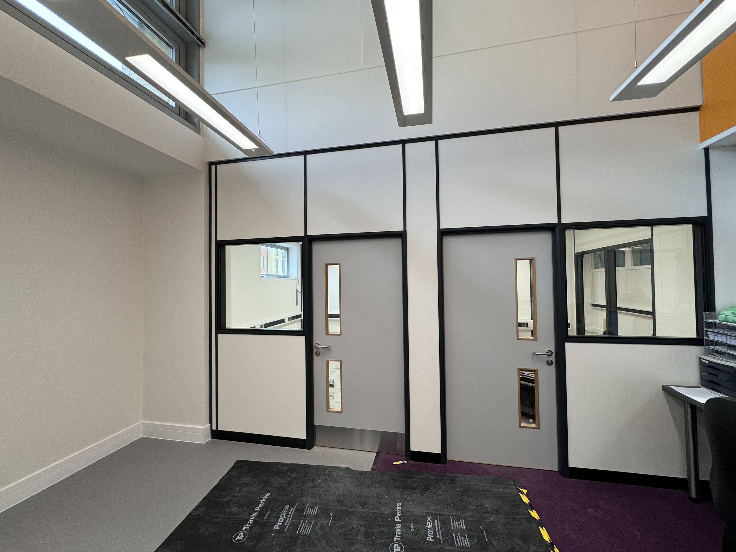 Interior of a modern office or clinic space with a glass partition, white walls, a window, and a black carpeted floor near the entrance.
