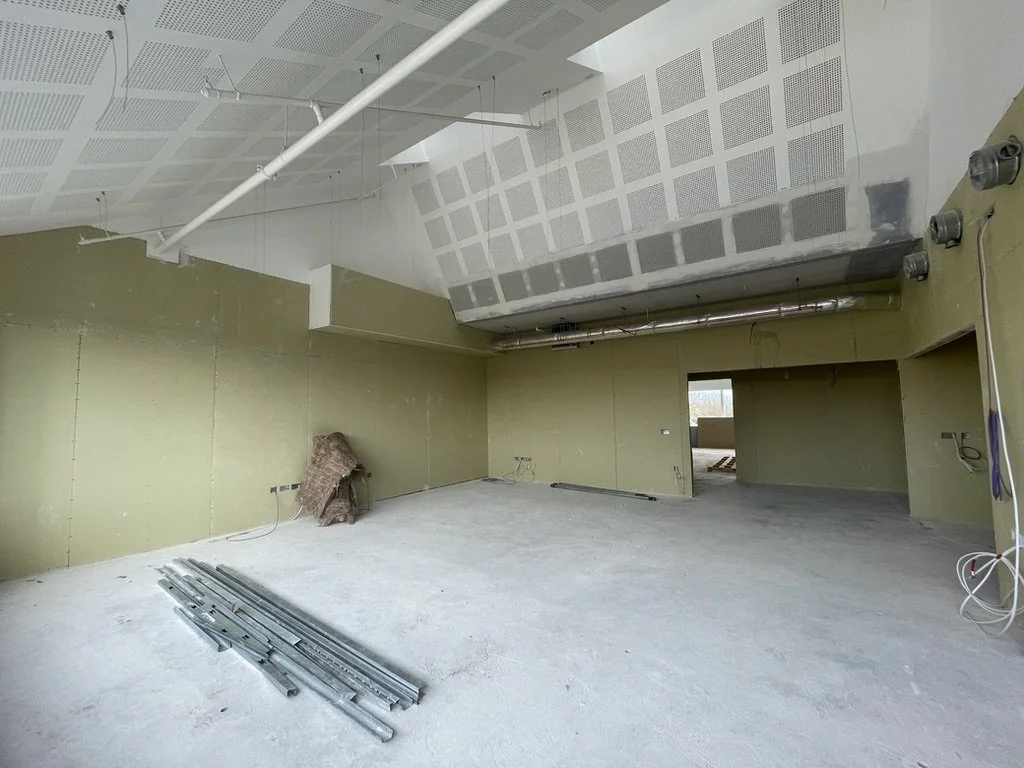 An unfinished room with green drywall on the walls, exposed ceiling with ventilation ducts, and construction materials on the floor.