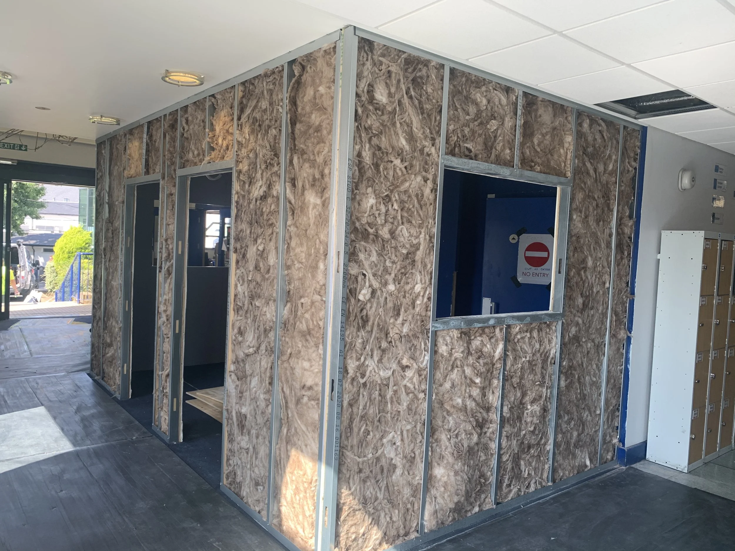 Interior of a building under construction with framed walls covered in insulation material, windows, and a partially open ceiling.